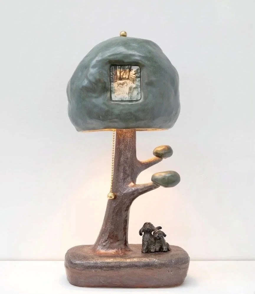 Decorative sculpture of a tree with a small dog at base, a branch with two leaves, and a large green rock formation with a mirror or window in the center, set against a plain background.