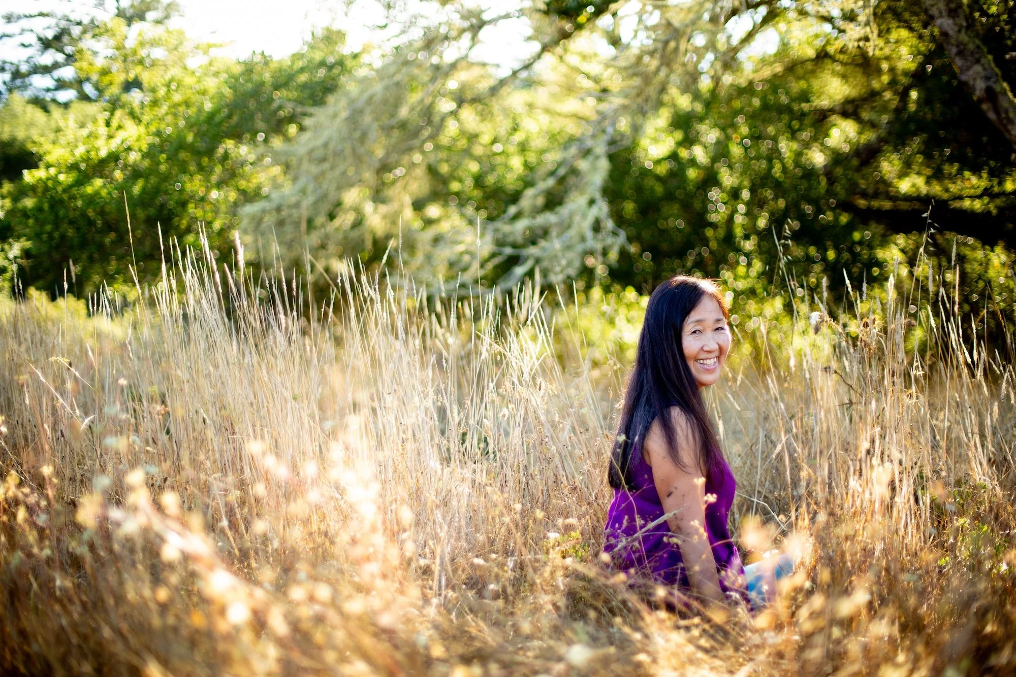 woman with dark hair sitting in a field under a tree