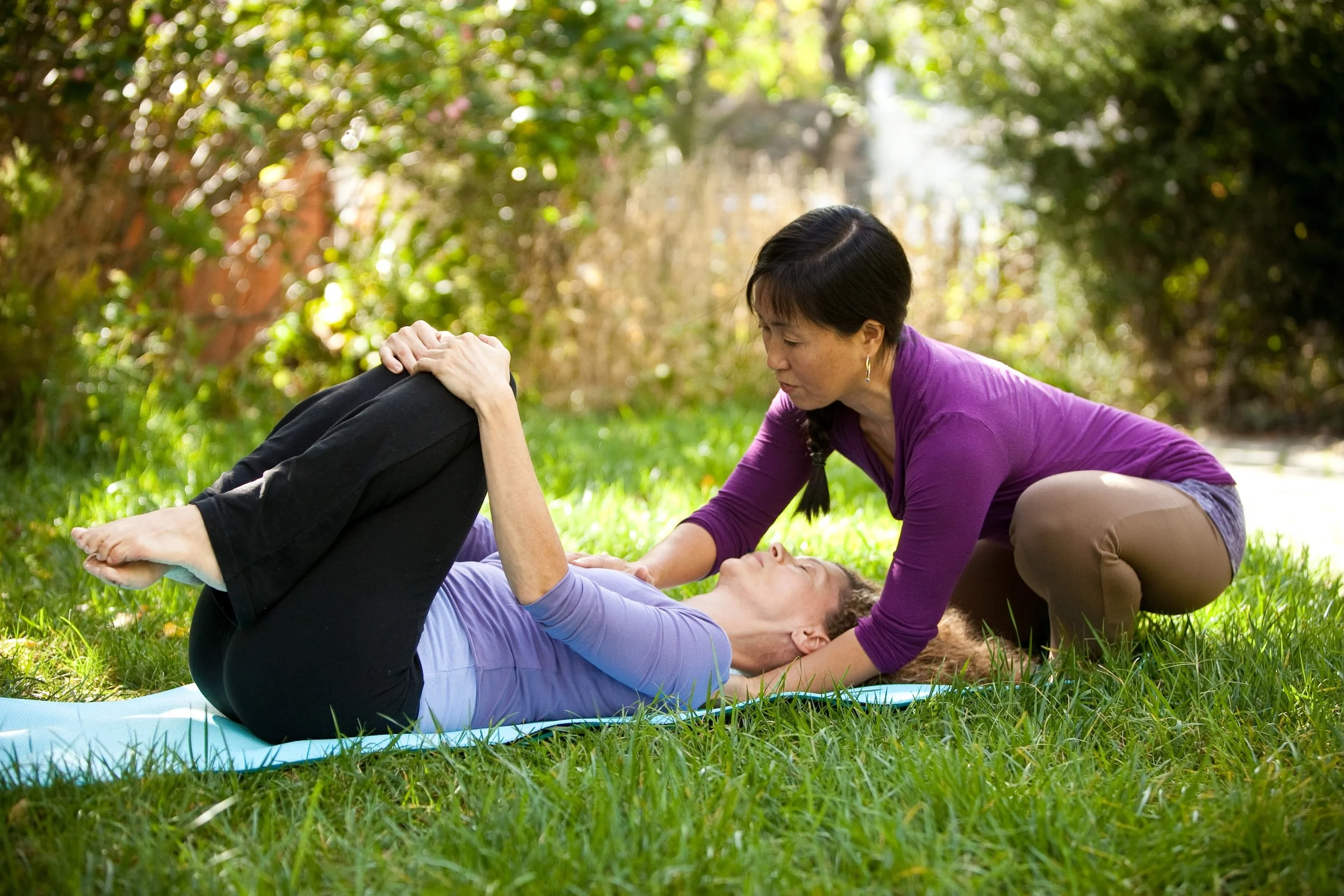 Yasue Tanaka gently supporting a client’s head and neck during an outdoor yoga therapy session.