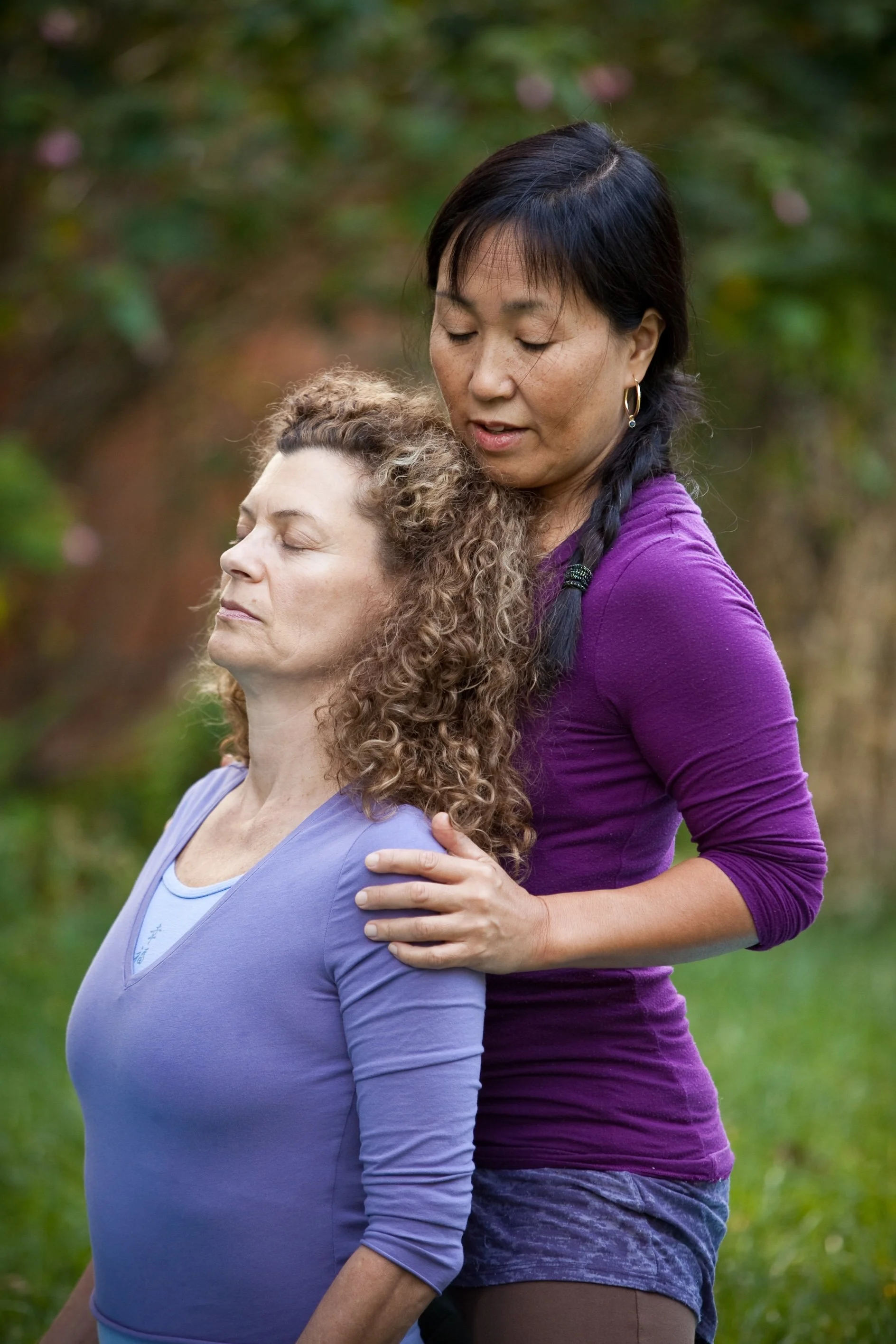 Yasue Tanaka gently supporting a client’s shoulders during an outdoor yoga therapy session.