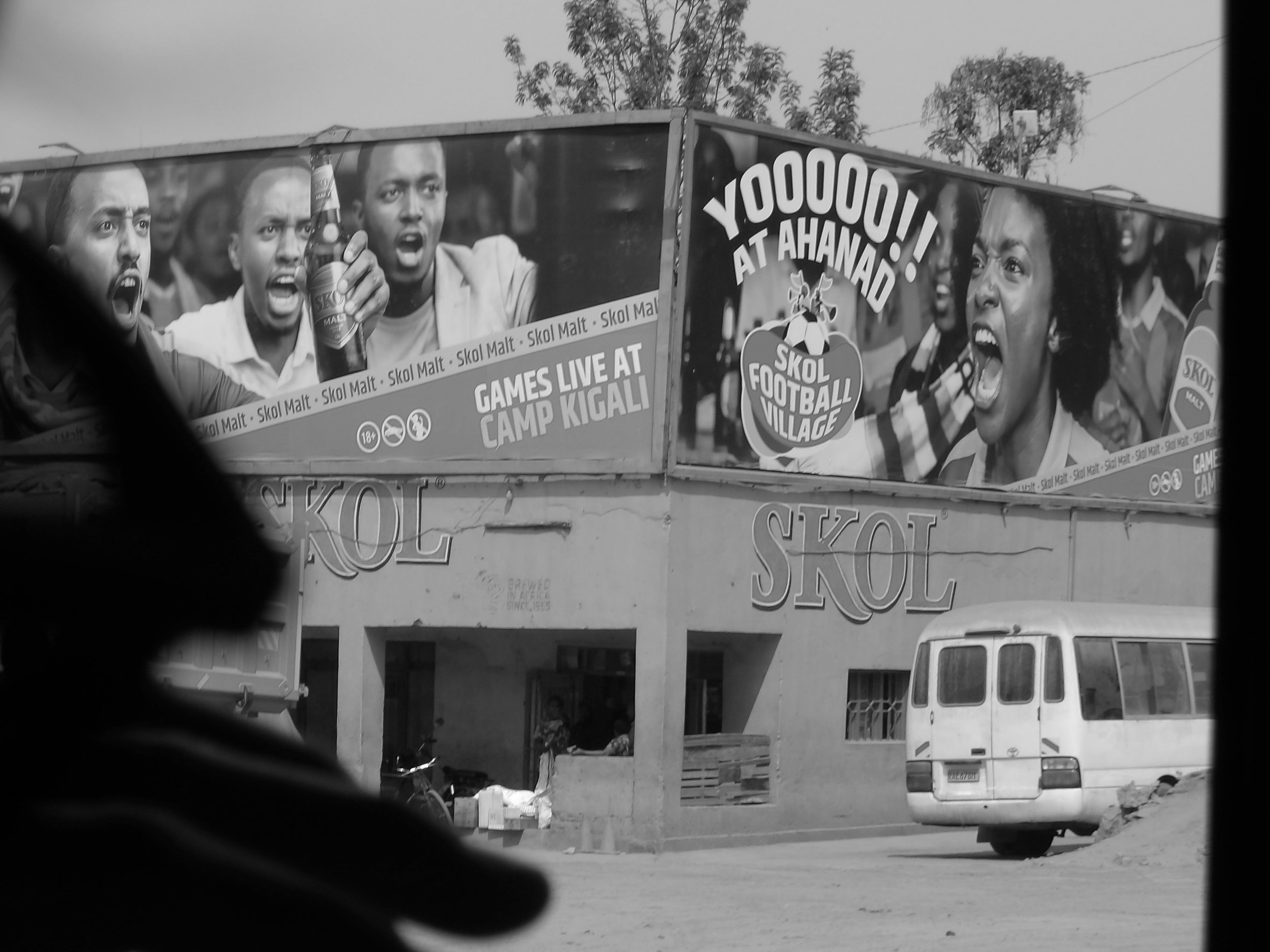 A billboard advertising football games at Camp Kigali featuring images of four people, including two women and two men, one of whom is holding a bottle. The billboard promotes Skol Malt and Skol Football Village, with the headline "Yoohoo! At Ahand" 