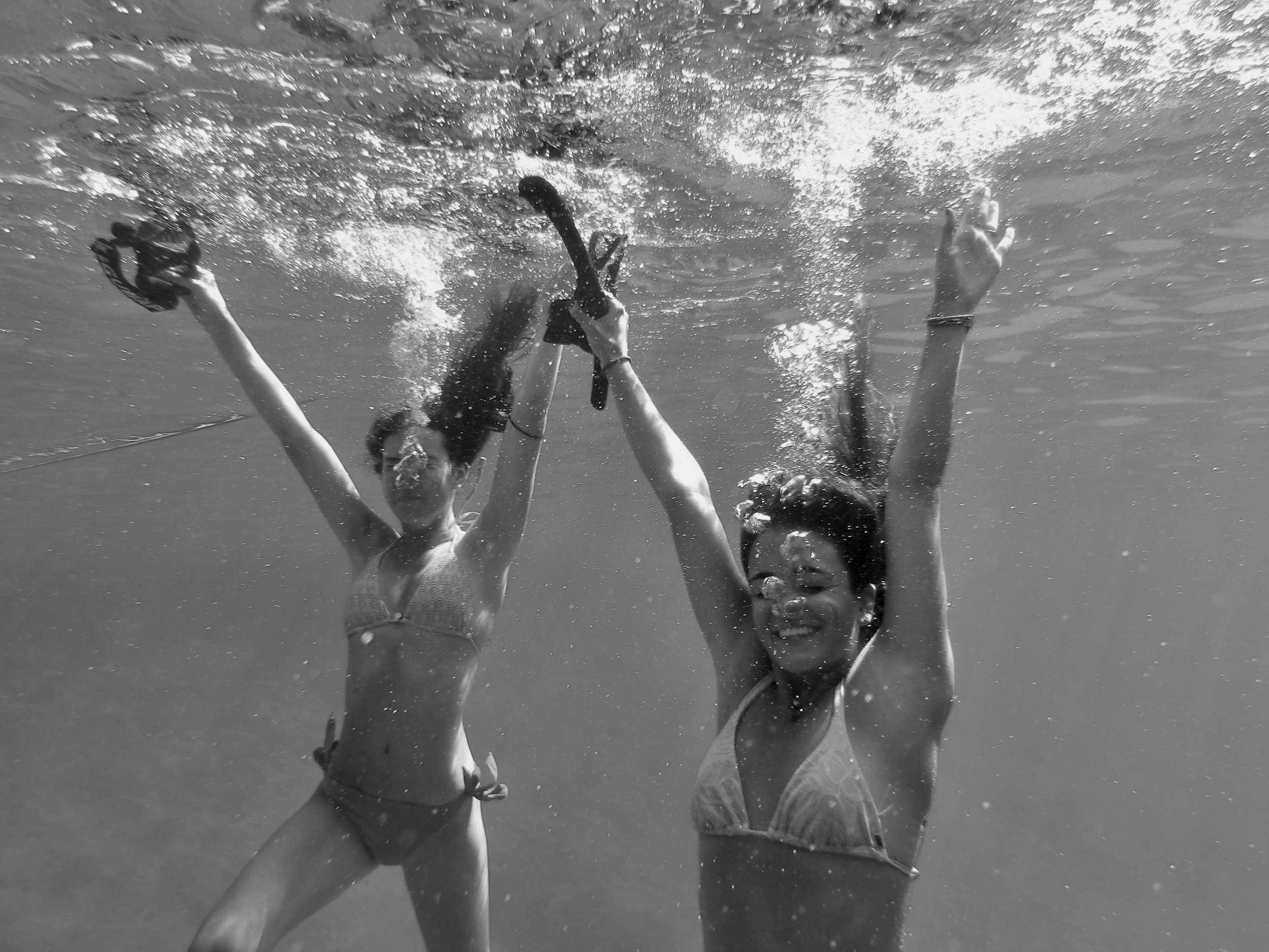 People underwater making peace signs with their hands, some holding snorkeling masks, in a black and white photo.
