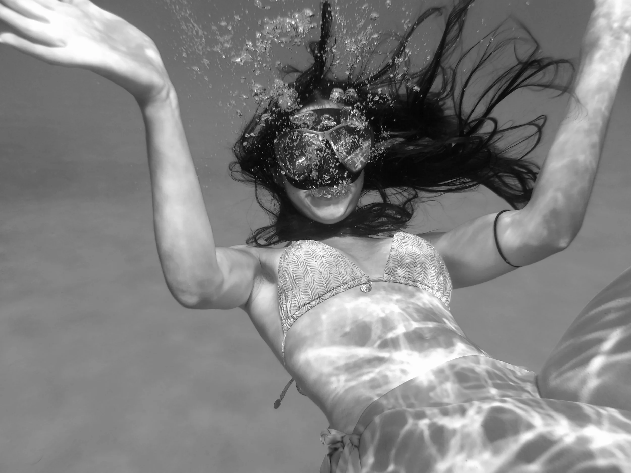 A woman submerged underwater, face partially visible with long hair flowing and bubbles around her.