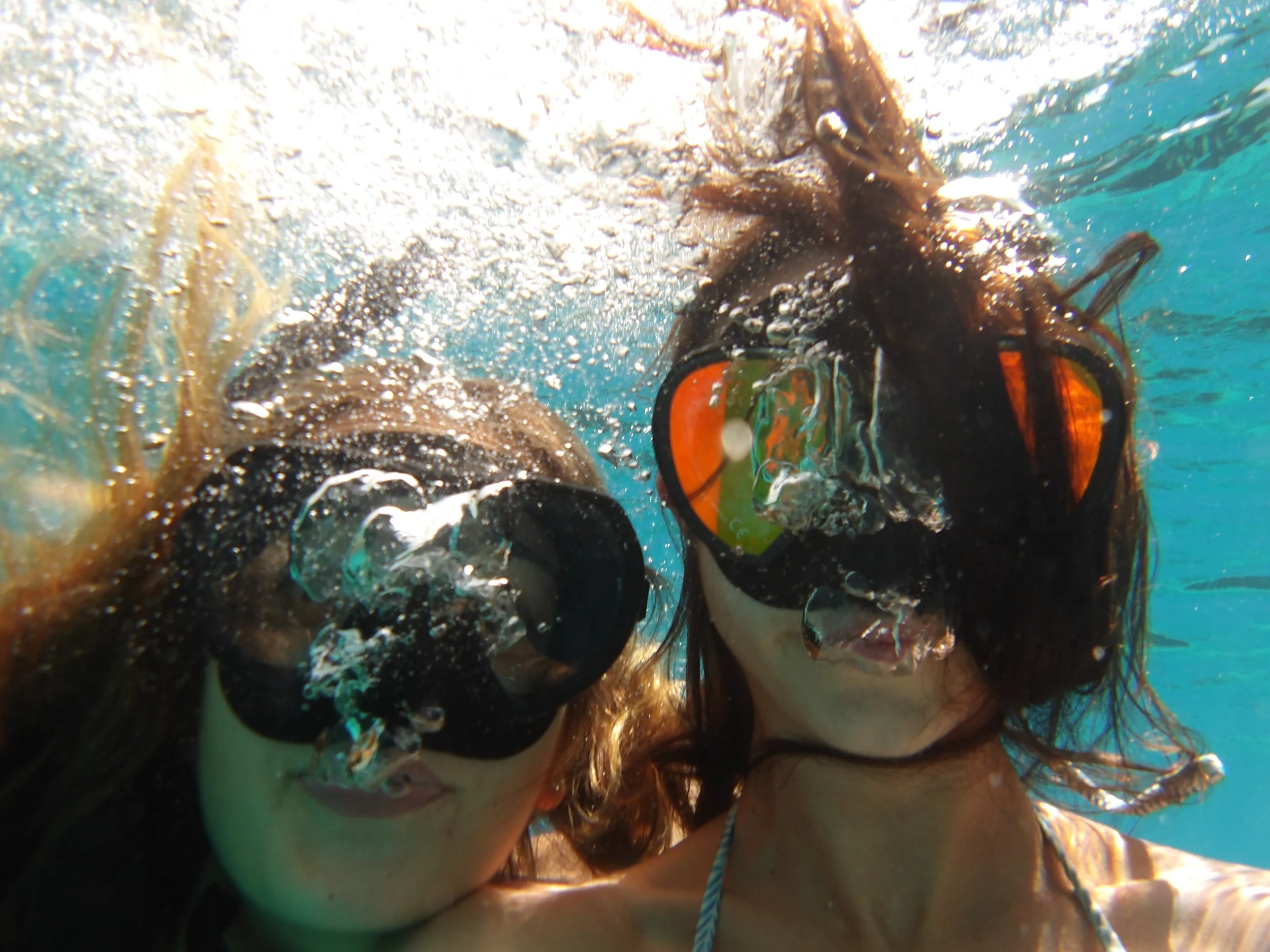 A person with underwater mask swimming, with sunlight visible and underwater plants in the background.
