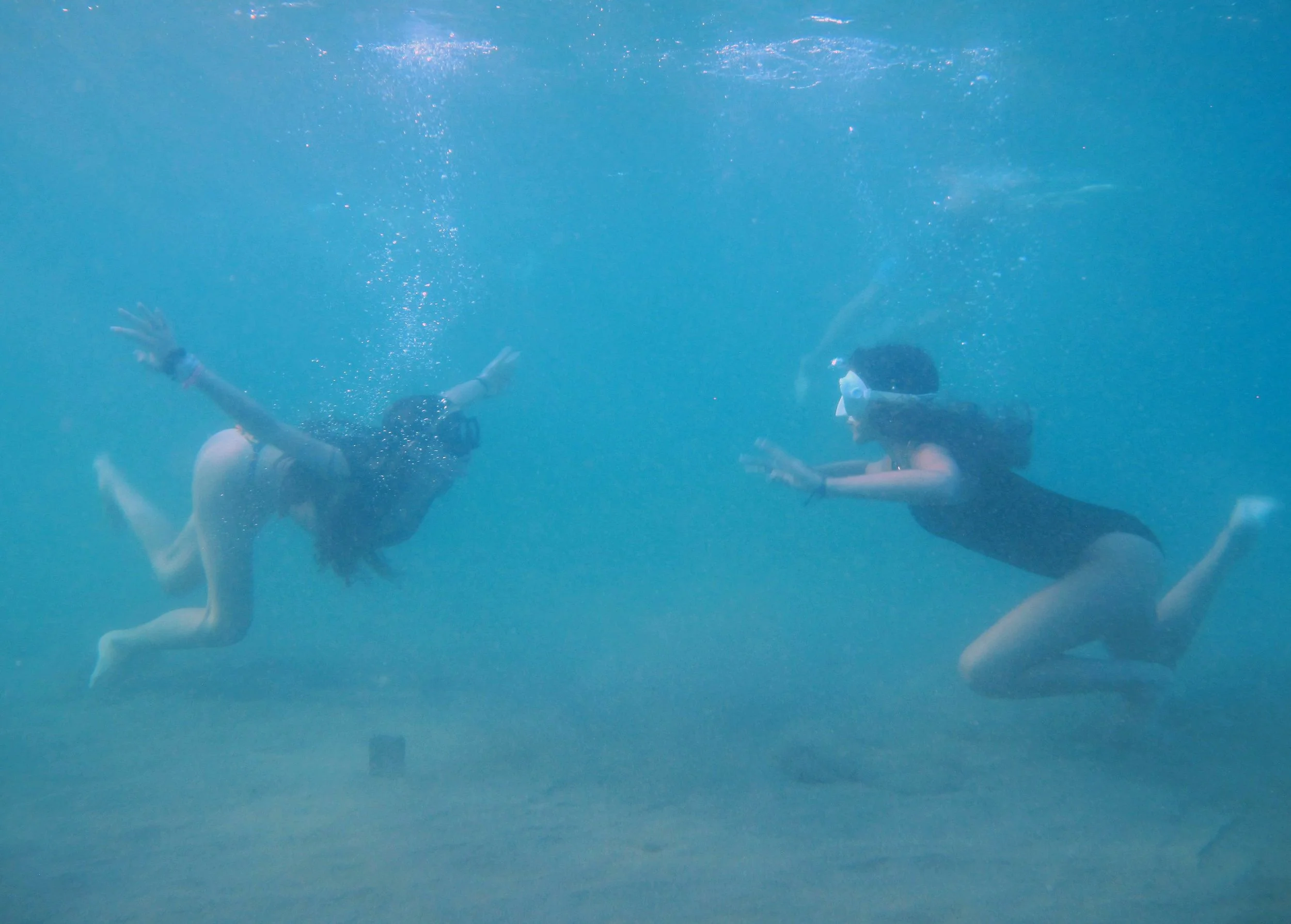 Two people underwater swimming towards each other, with bubbles surrounding them in the sea