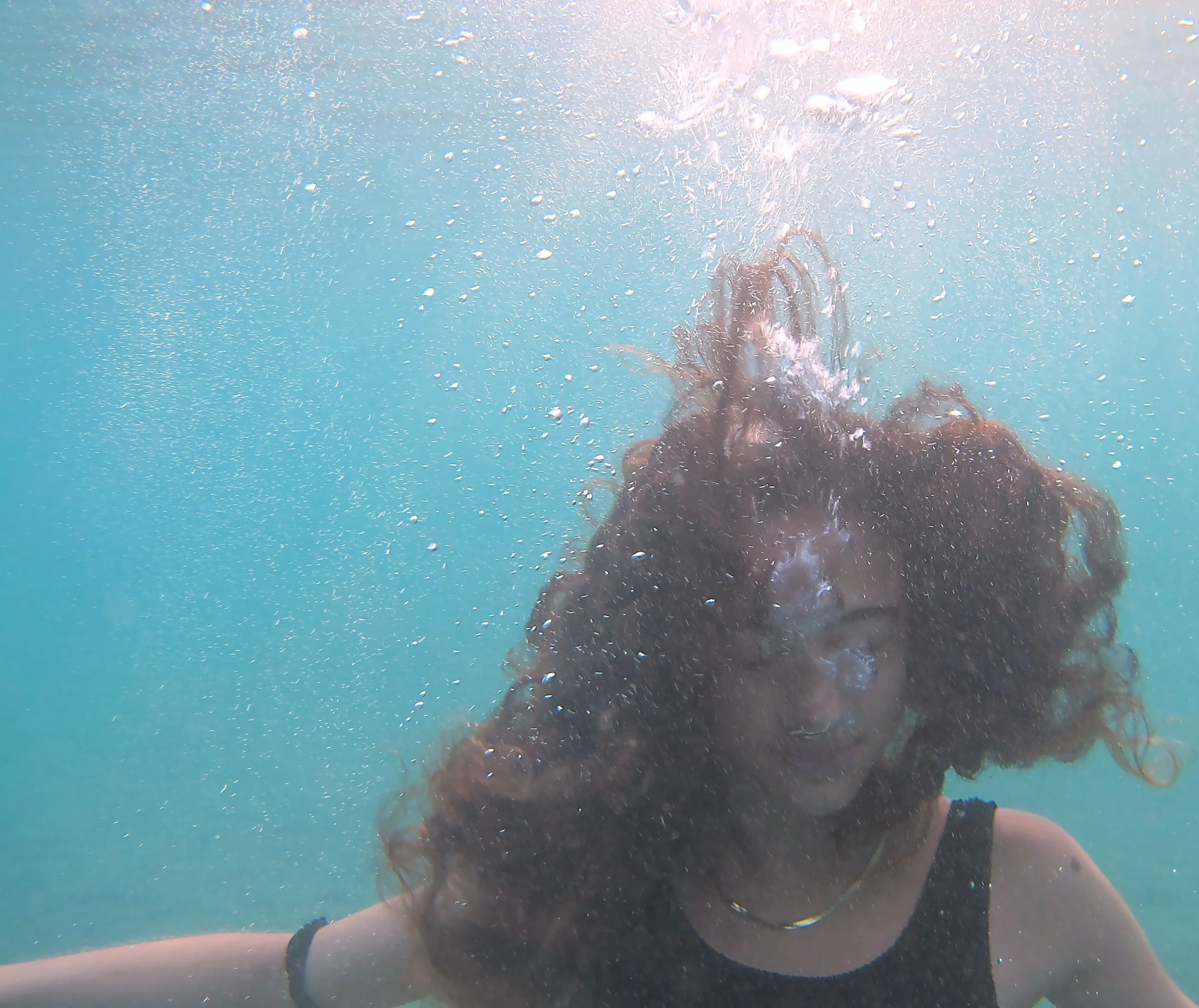 Person swimming underwater with bubbles surrounding them, visible legs, arm, and wristband.