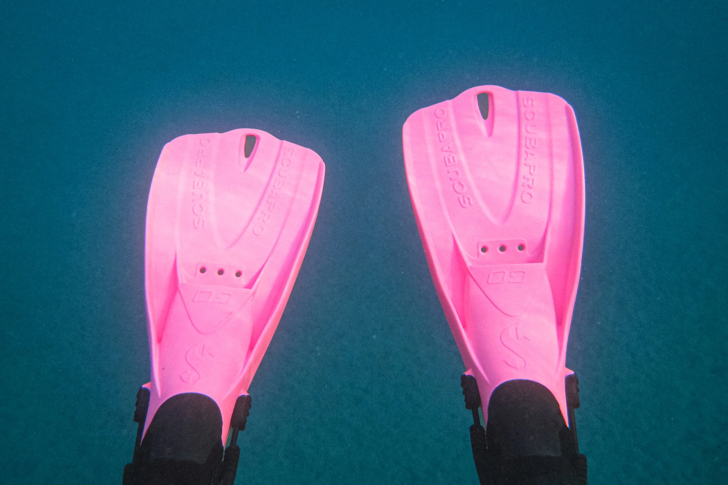 Pair of pink sports shoes worn by a person standing on a blue indoor court.