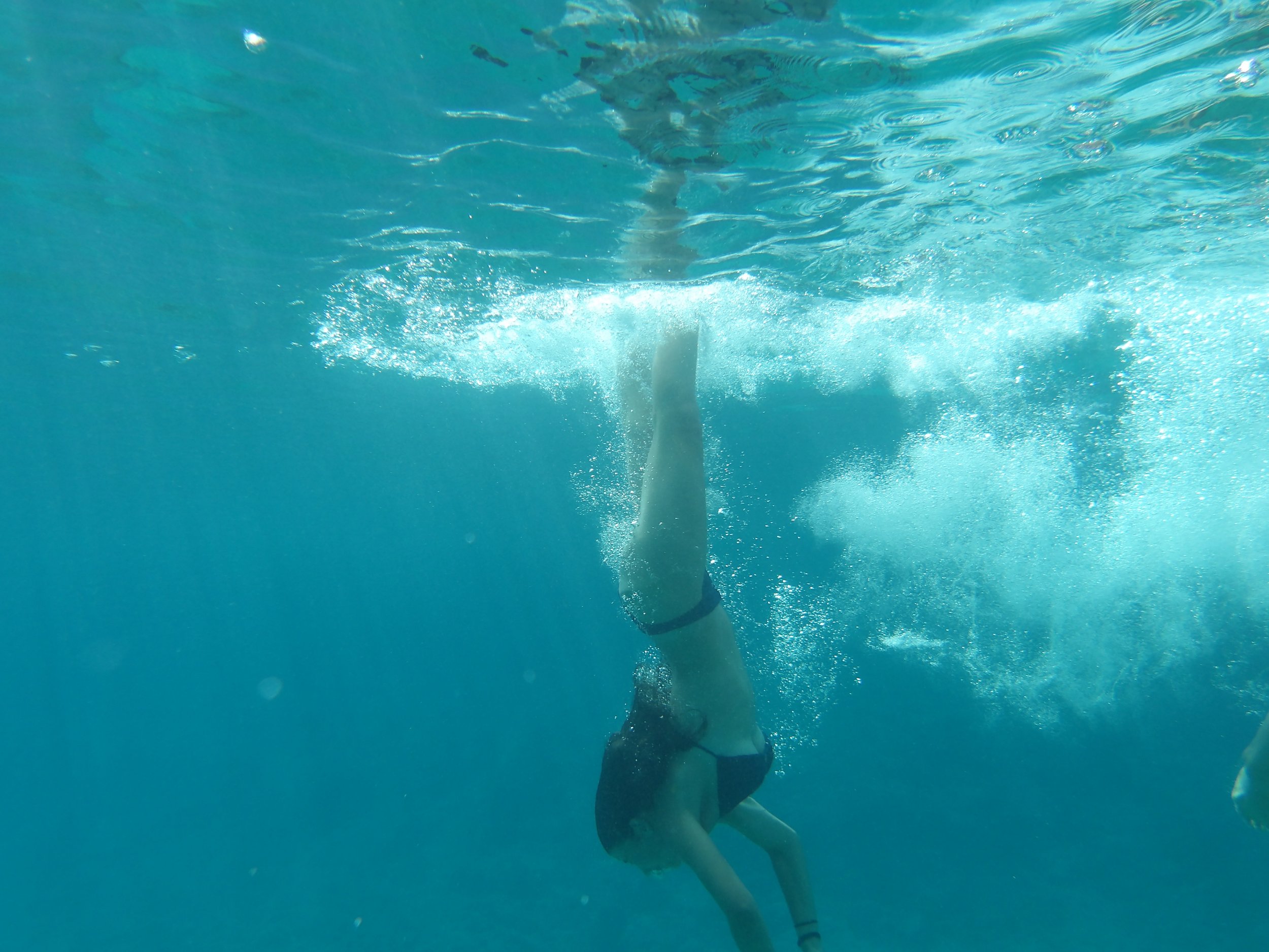 Person diving into turquoise swimming pool, water bubbles rising, poolside tiles visible at the top