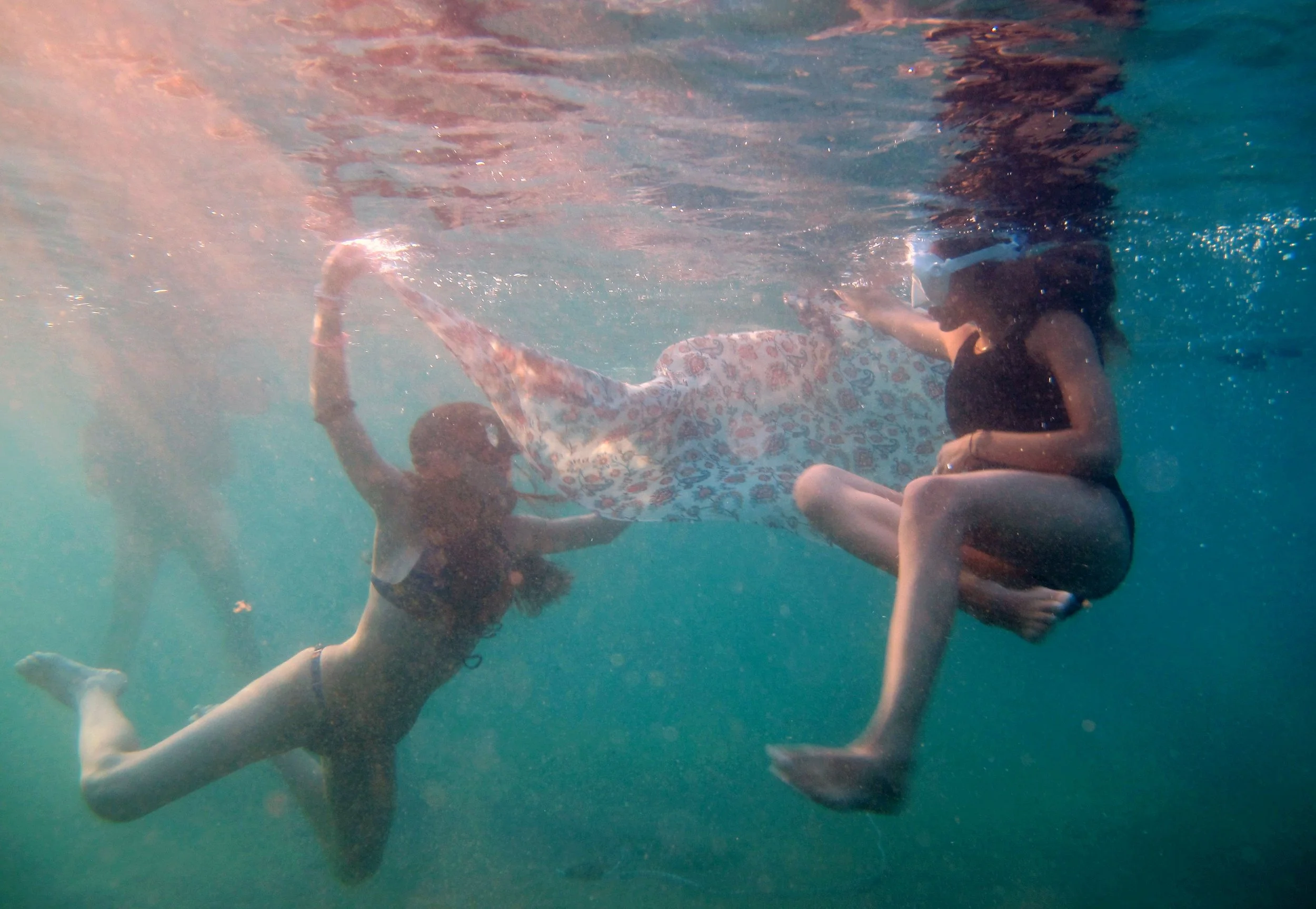 Two women underwater, swimming and holding hands, wearing swimsuits.