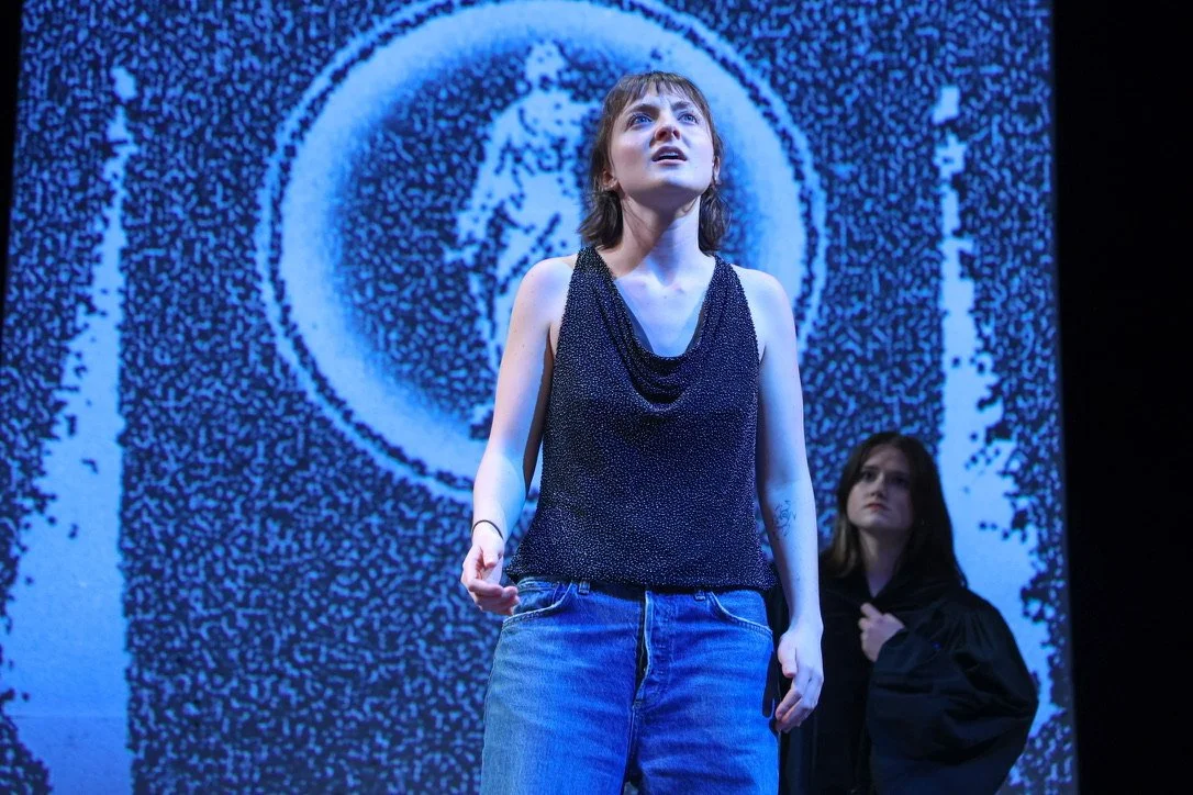 Two young women on stage with a large swirling blue and white abstract background projection.