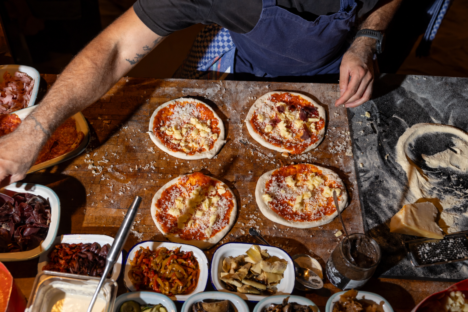 Four pizzas being prepared with fresh toppings.