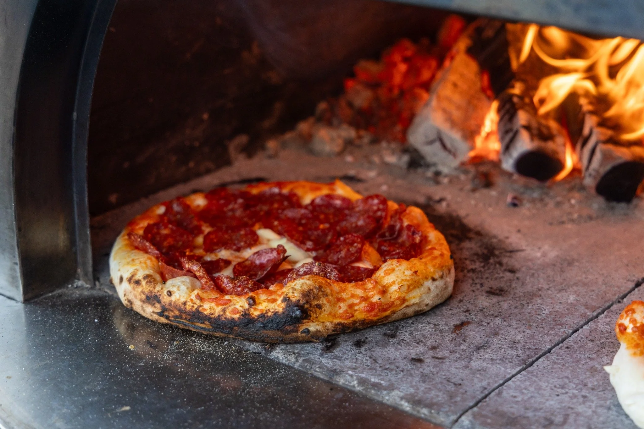 Pizza baking beside glowing wood embers.