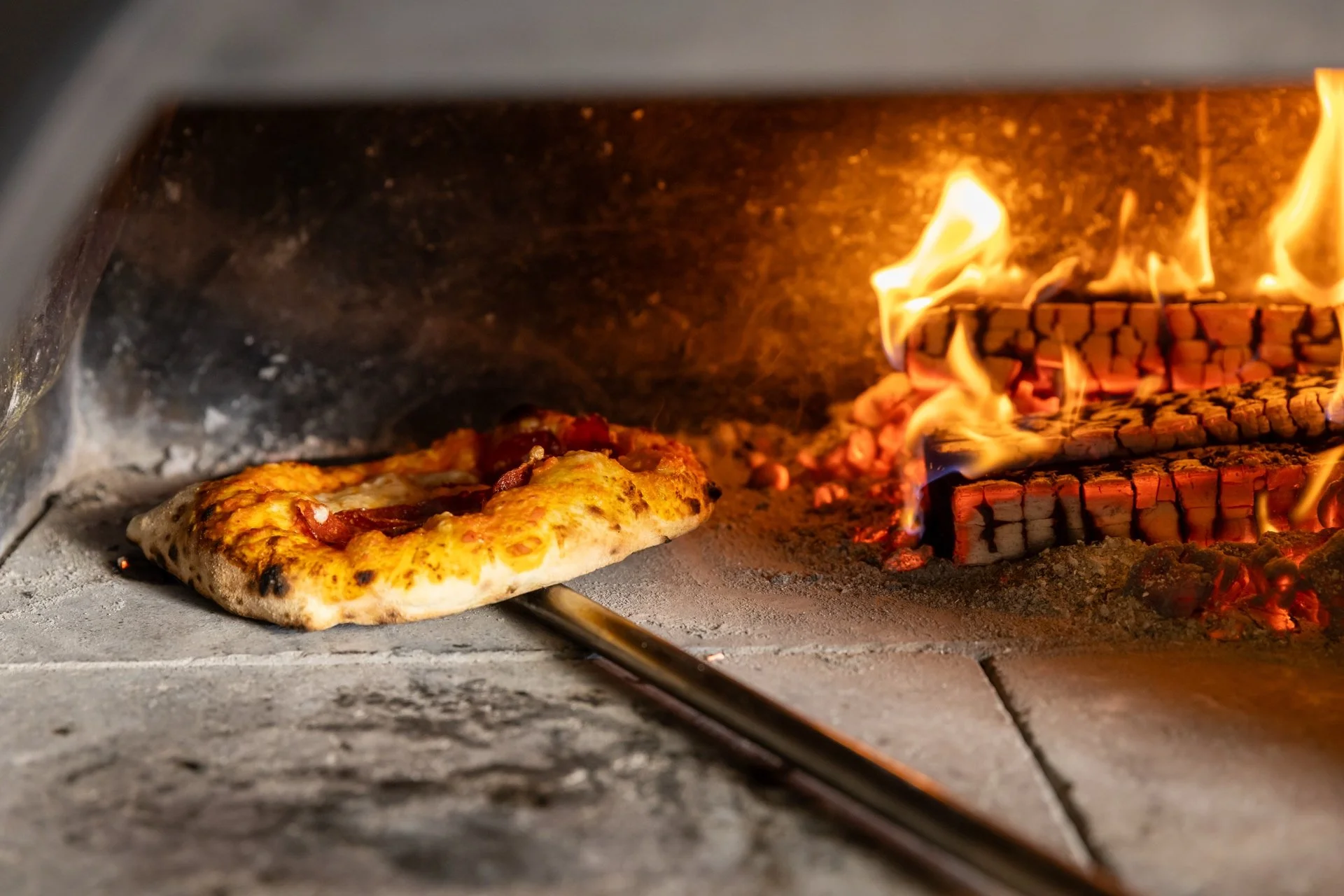 Pizza baking beside glowing logs in a wood-fired oven