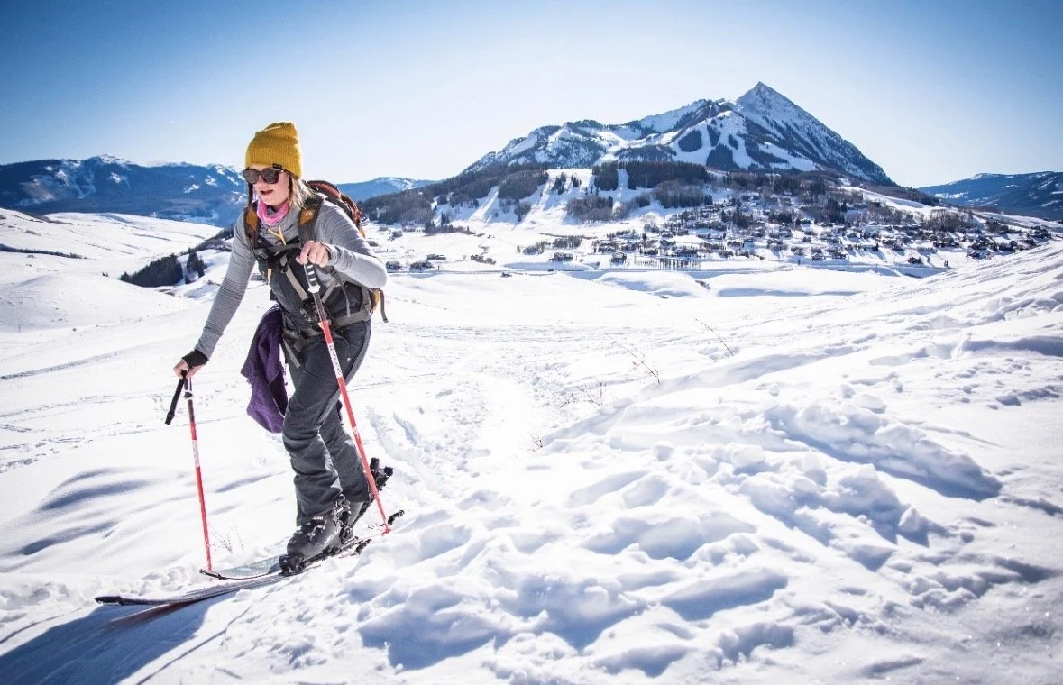 A woman skiing in a snowy mountain landscape with a clear blue sky and a mountain in the background.