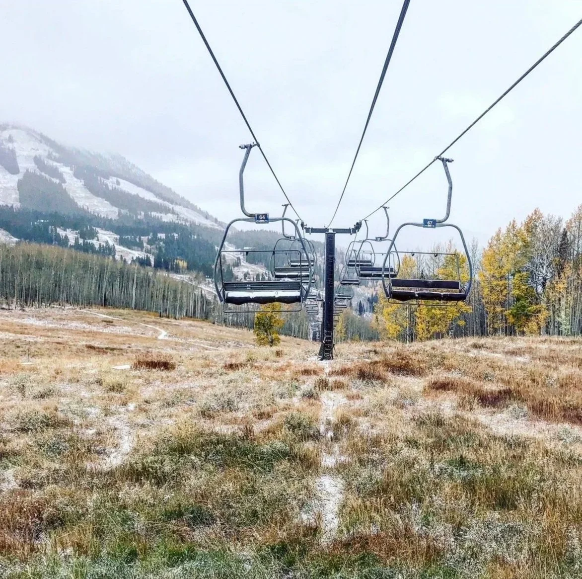 Empty ski chairlift on a mountain with frosted grassy field and trees, cloudy sky in autumn.