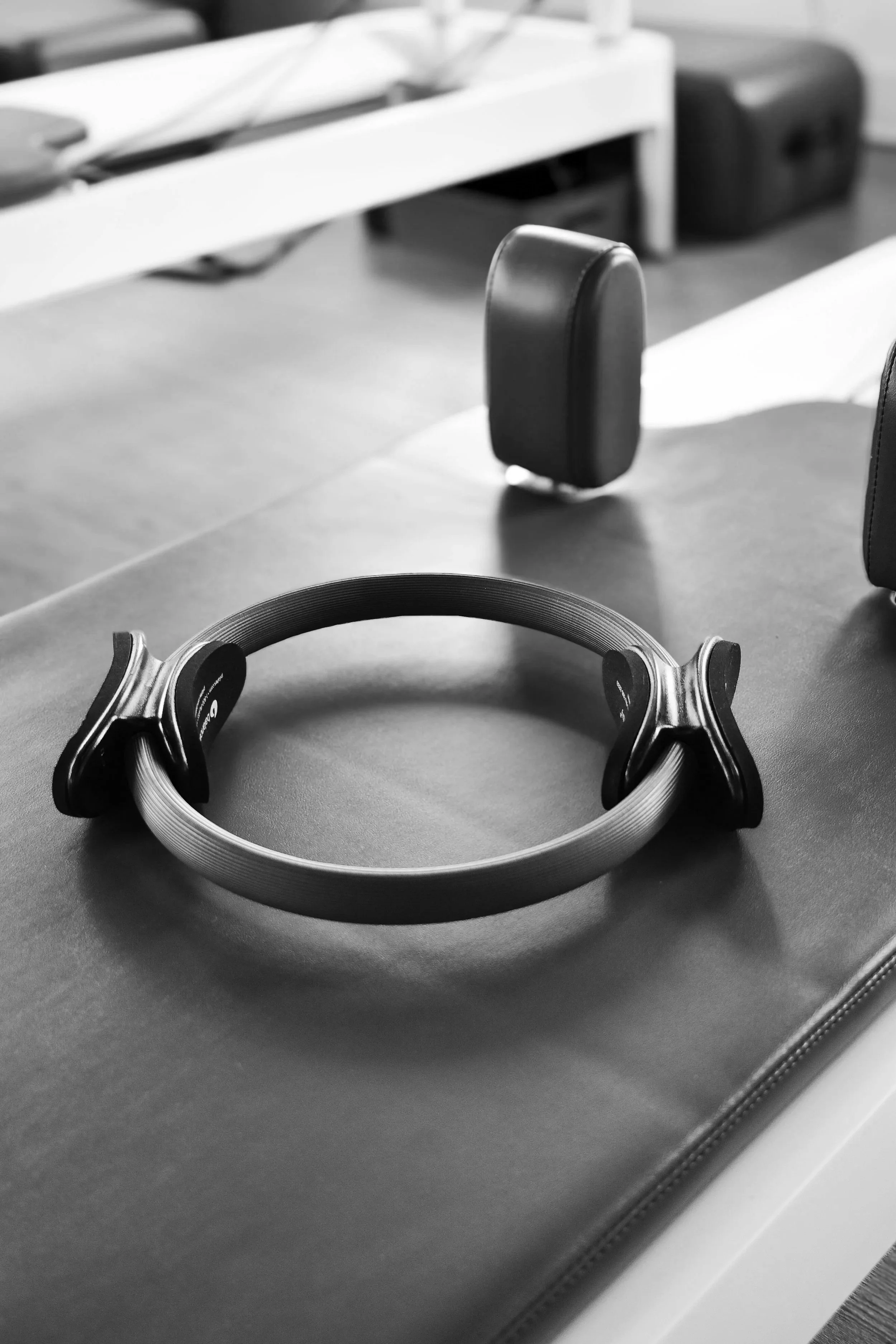 Black and white photo of a pair of headphones on a table, with the headband facing up and the ear cups facing down, near a blurred background with a headphone stand.