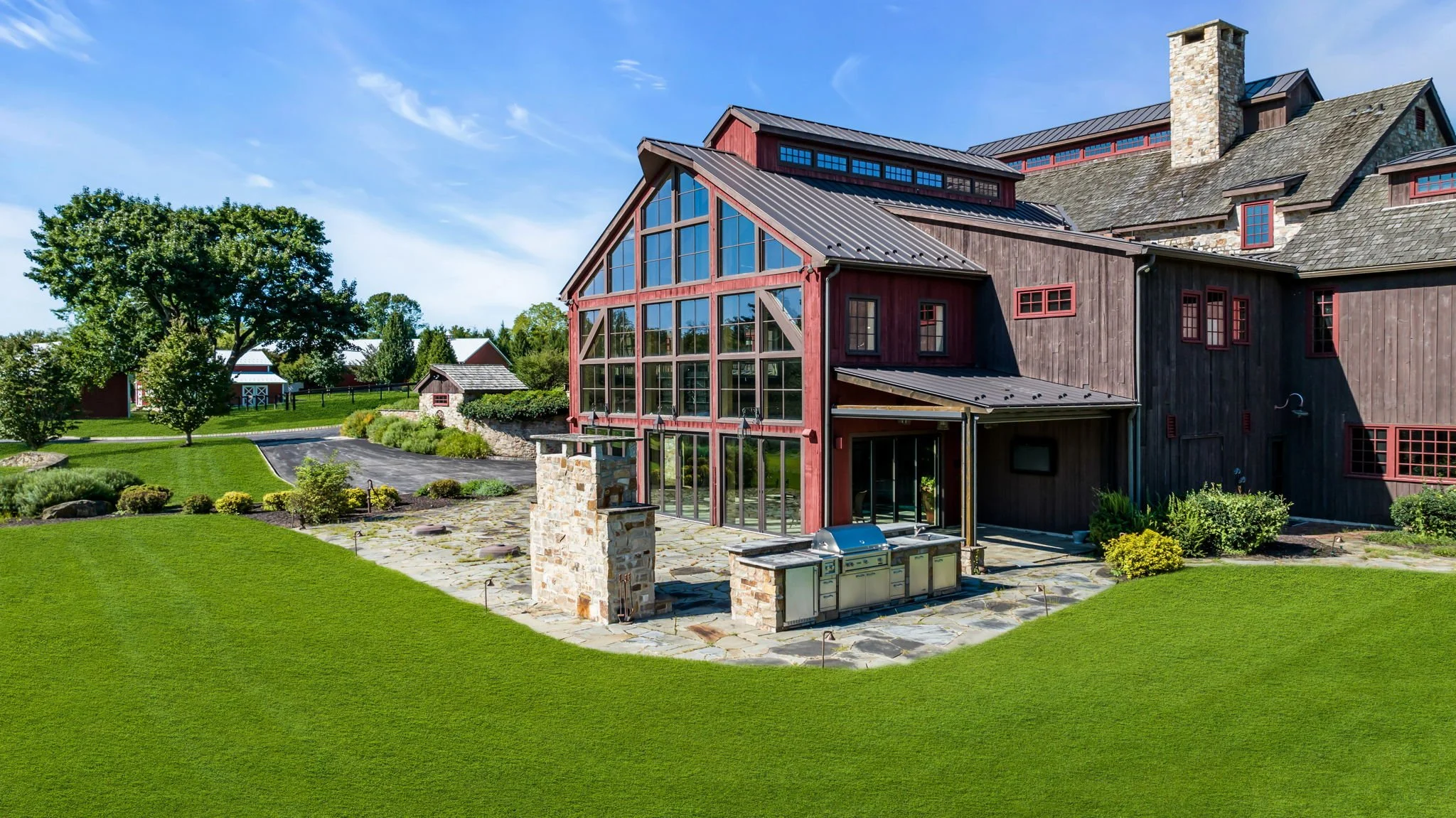 A large house with wooden siding, a prominent glass enclosed porch, and a stone chimney, surrounded by a well-maintained lawn and landscaping under a blue sky.