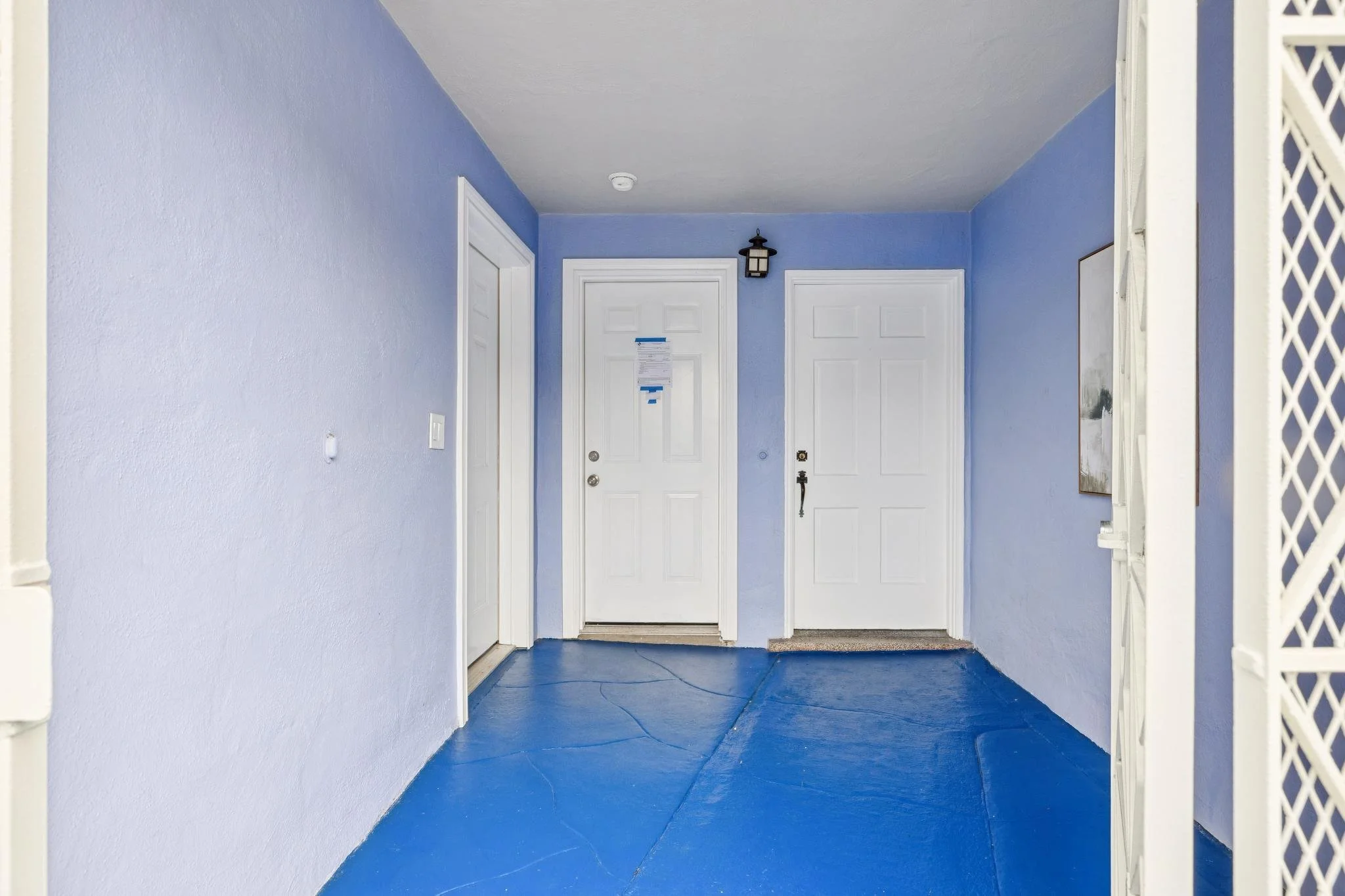 Entryway with light blue painted walls, white doors, a doorbell and a black wall lantern light fixture, with a smart thermostat on the left wall, a framed mirror on the right wall, and a dark gray carpeted floor.