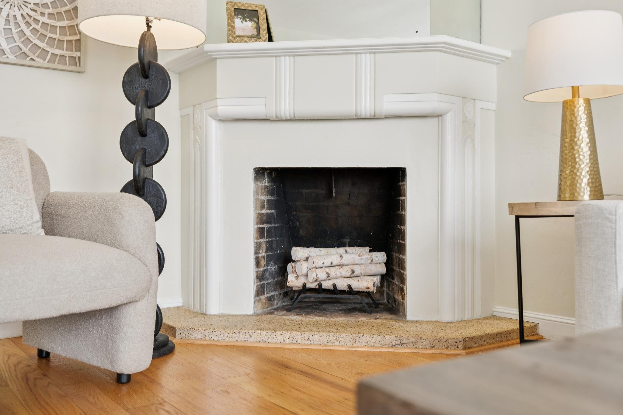 Living room with a white fireplace, beige armchair, a side table with a gold textured lamp, and two table lamps on the walls, one on each side of the fireplace.