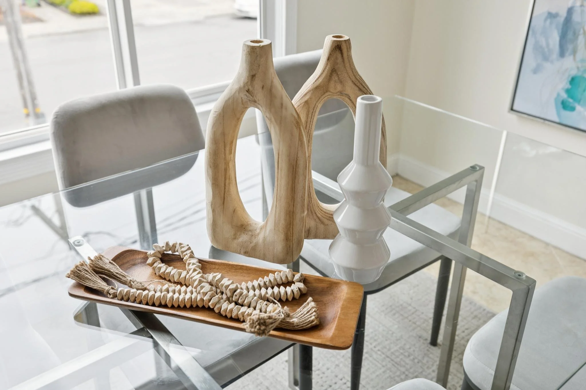Decorative vases with natural wood and white ceramic designs on glass table near window with a view of the street outside.