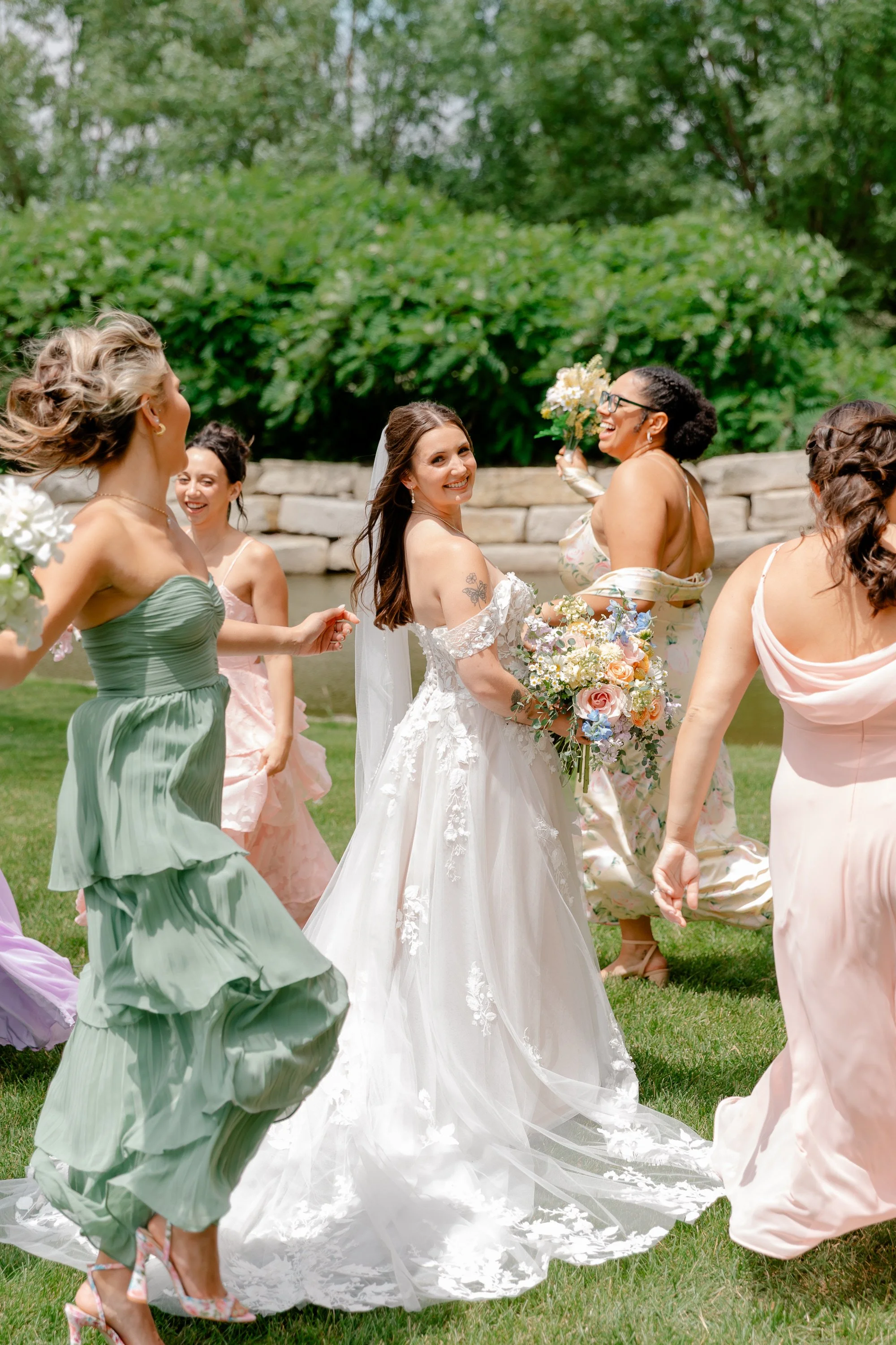 Group of women, including a bride in a white wedding dress, dancing and smiling outdoors during a wedding celebration.