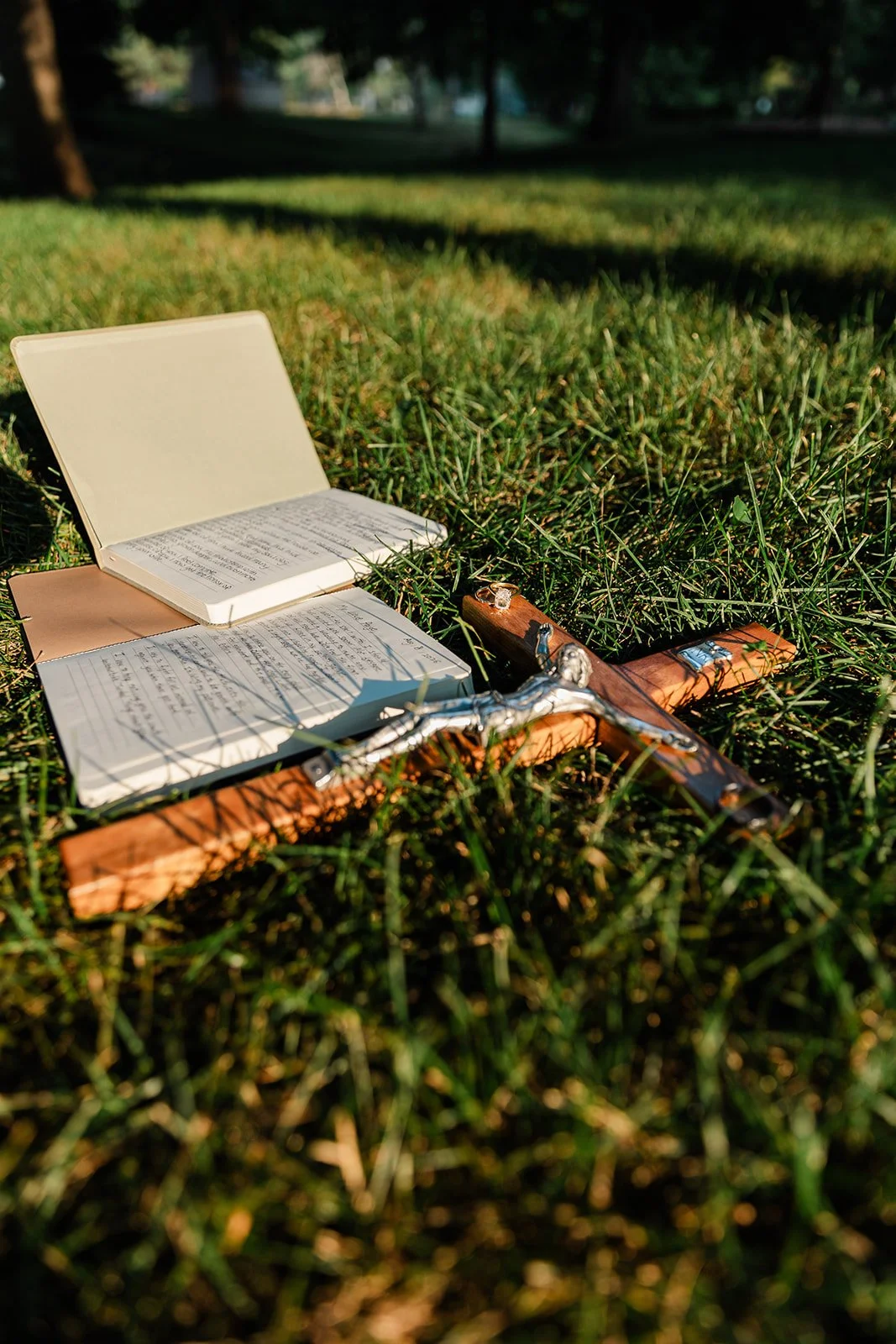 Open prayer book, notes, and crucifix on the grass in a park.