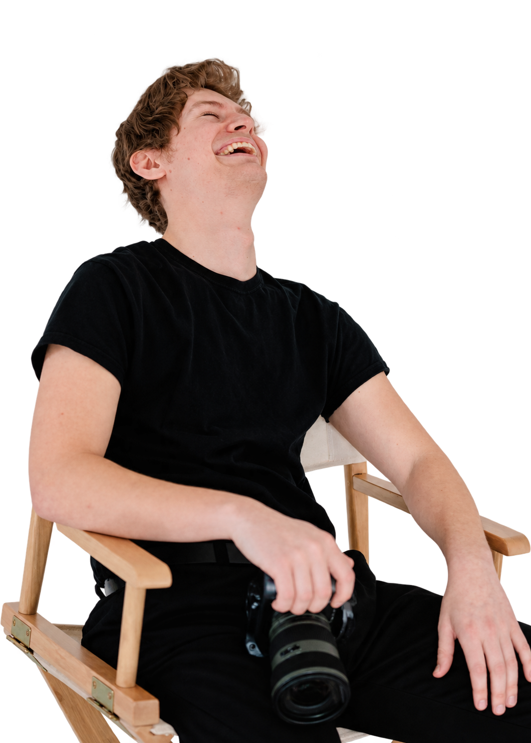 Young man sitting in a wooden chair with a camera, smiling and looking upwards.