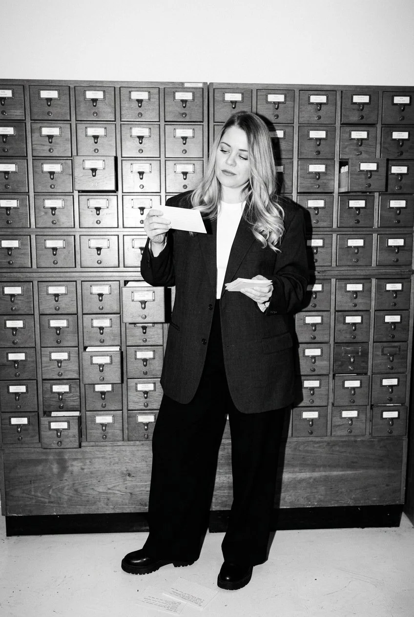 A woman in business attire looking at a piece of paper in front of a row of mailbox lockers.