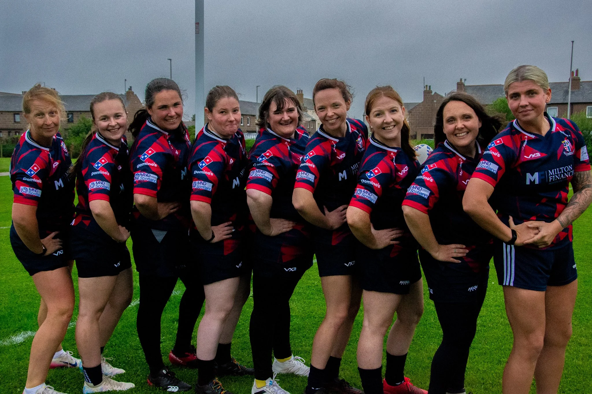Rugby players standing together in a diagonal line, smiling towards the camera.