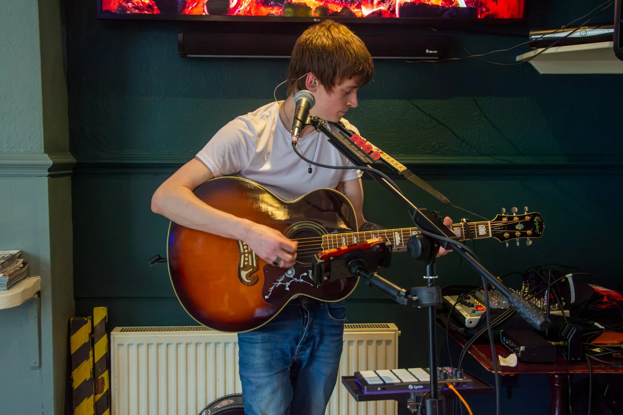 Musician looking down while playing an acoustic guitar beside a microphone.