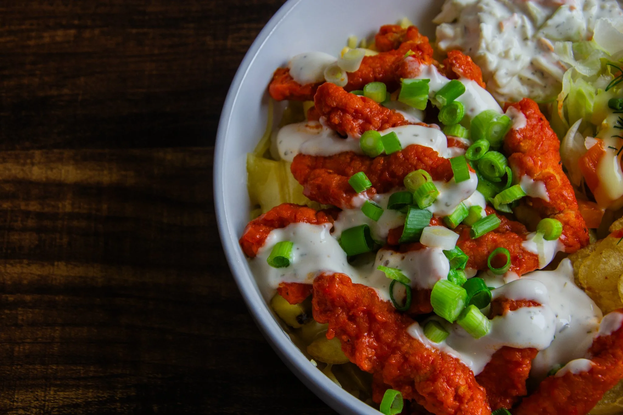 Close-up of chicken pieces over chips, topped with white sauce and chopped spring onions.