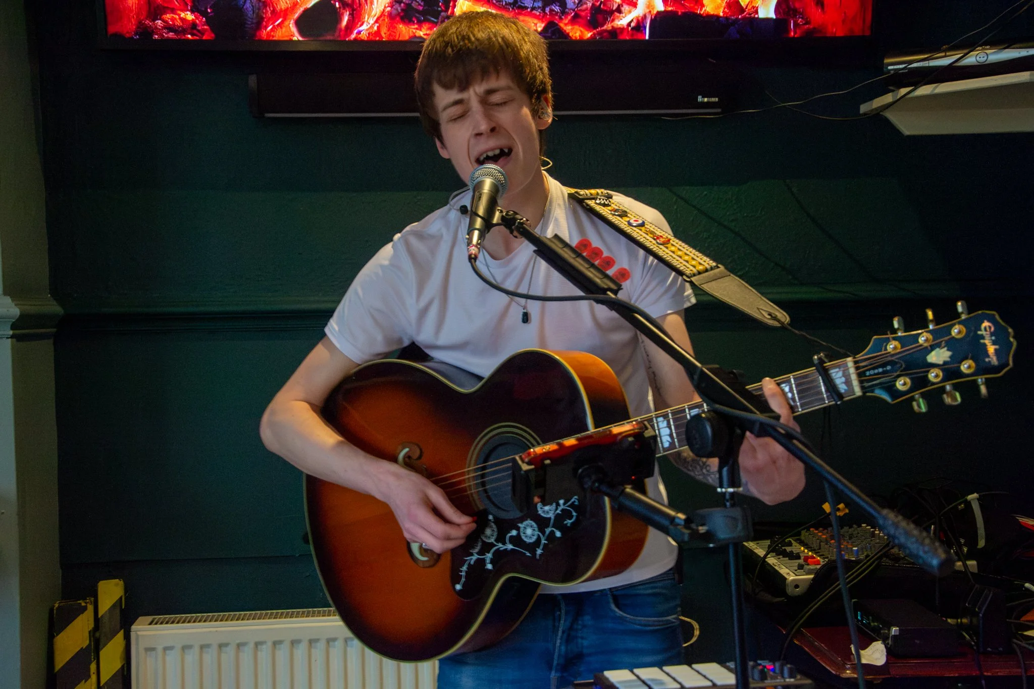 Musician singing into a microphone with eyes closed while playing an acoustic guitar.