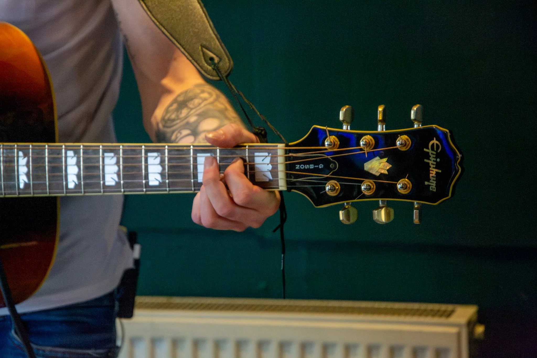 Close-up of a musician’s hand holding a chord on an acoustic guitar.