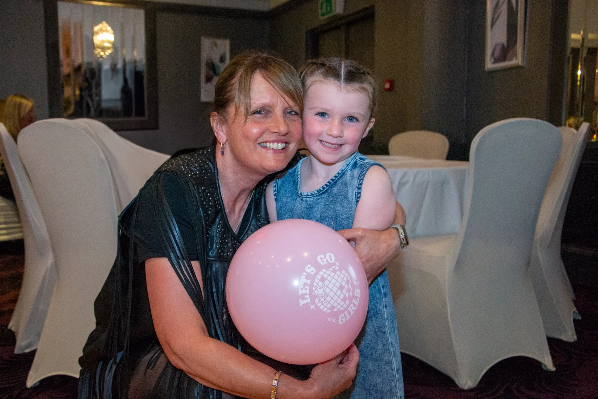 Woman and young girl smiling together at a celebration, holding a pink balloon.