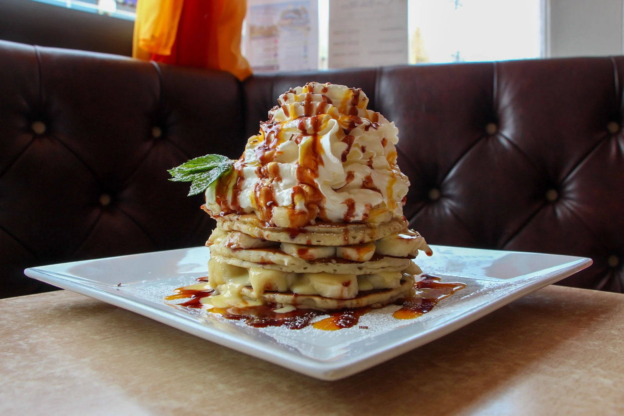 Stack of pancakes layered with banana and topped with whipped cream and drizzled sauce.