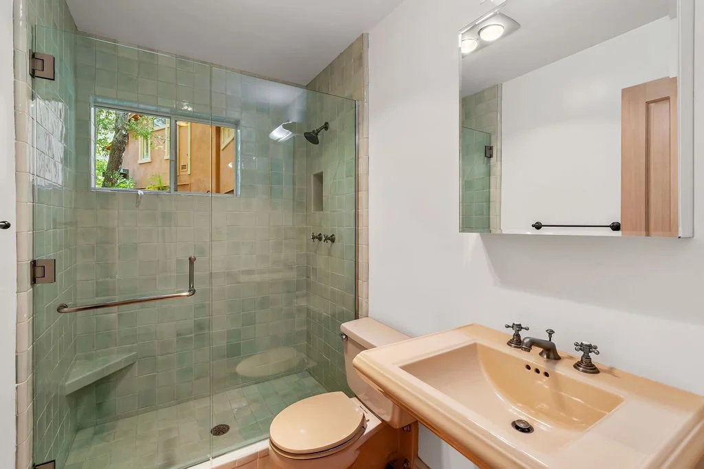 Bathroom with a beige sink, a large mirror, and a shower with frosted glass door and a window showing trees outside.
