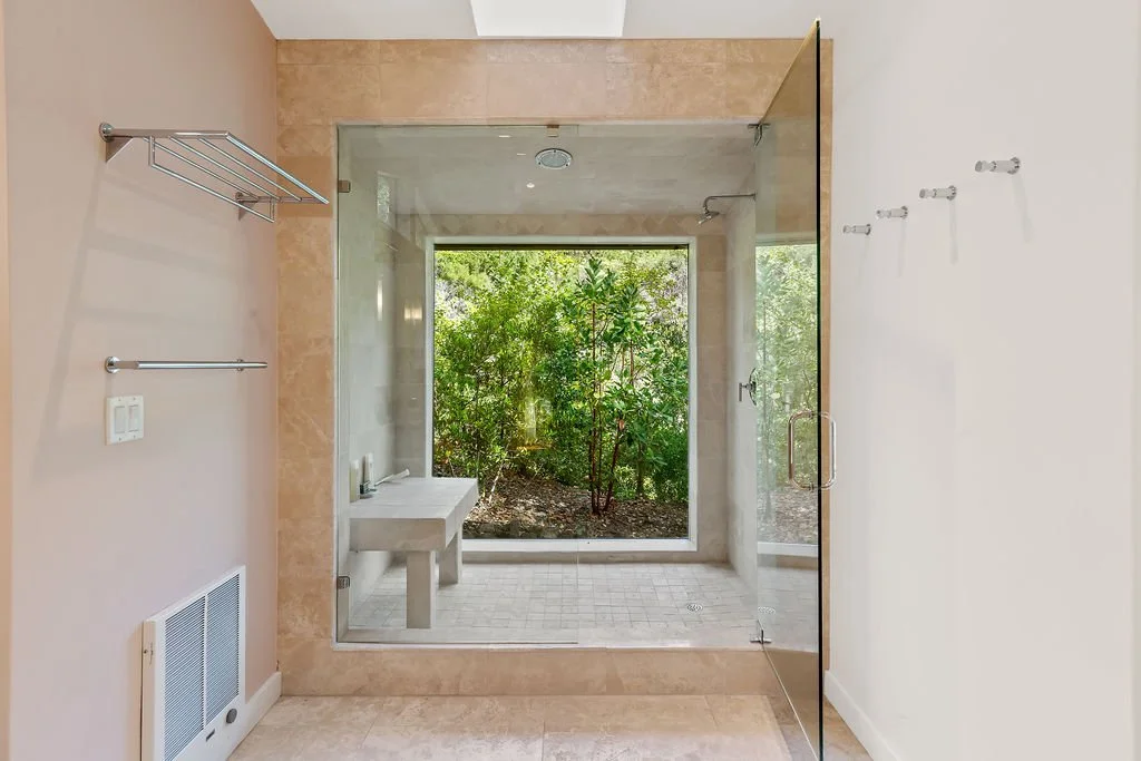 Bathroom with a large glass shower enclosure and a view of greenery outside through a large window.