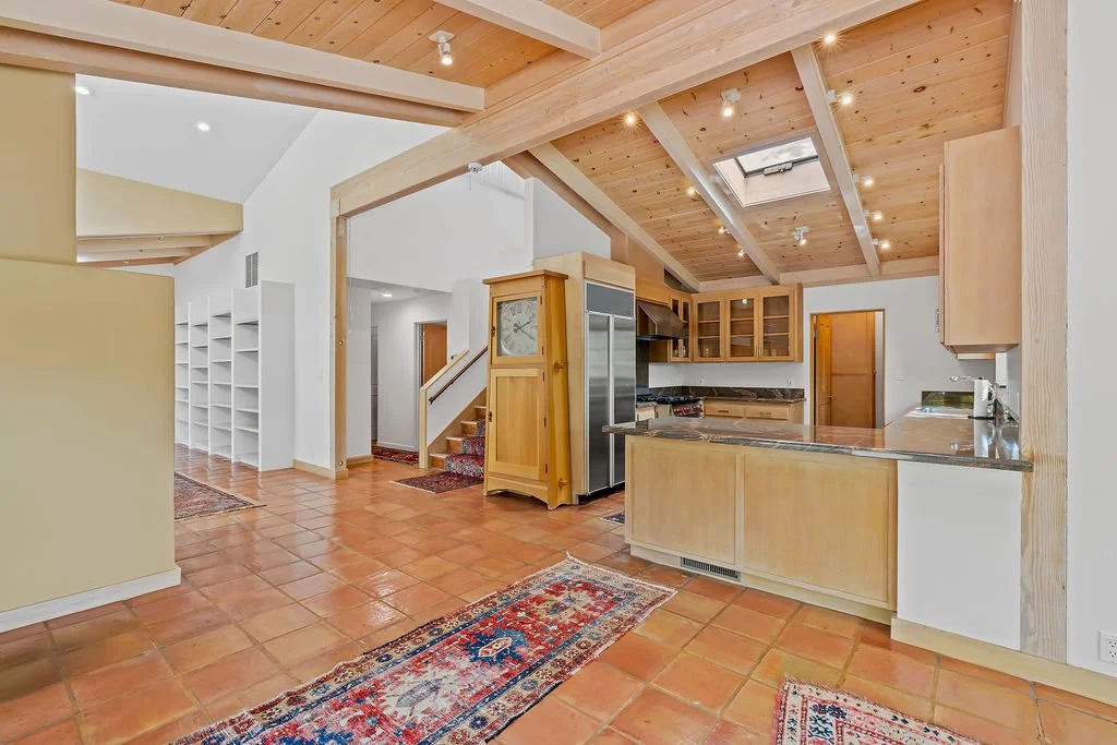 Open-concept kitchen with wood cabinets, stainless steel appliances, granite countertops, terracotta tile floor, recessed lighting, and a skylight in the beamed wooden ceiling.