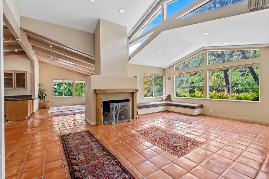 Spacious living room with large windows, a built-in stone fireplace, terracotta tile floors, and a cozy corner window seat.