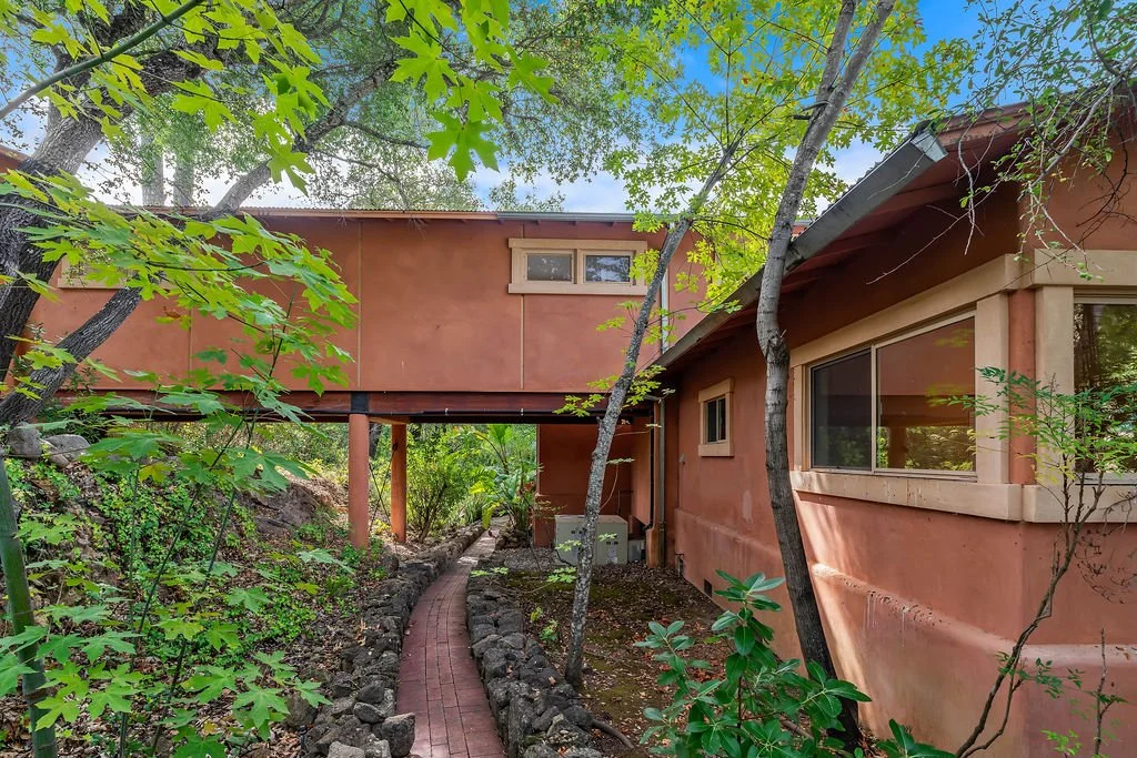 A house with a pathway leading to the side, surrounded by trees and greenery.