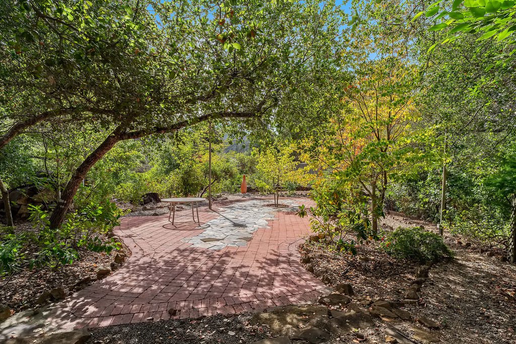 Garden with a winding brick pathway, trees with green and yellow leaves, and a small table in the background.