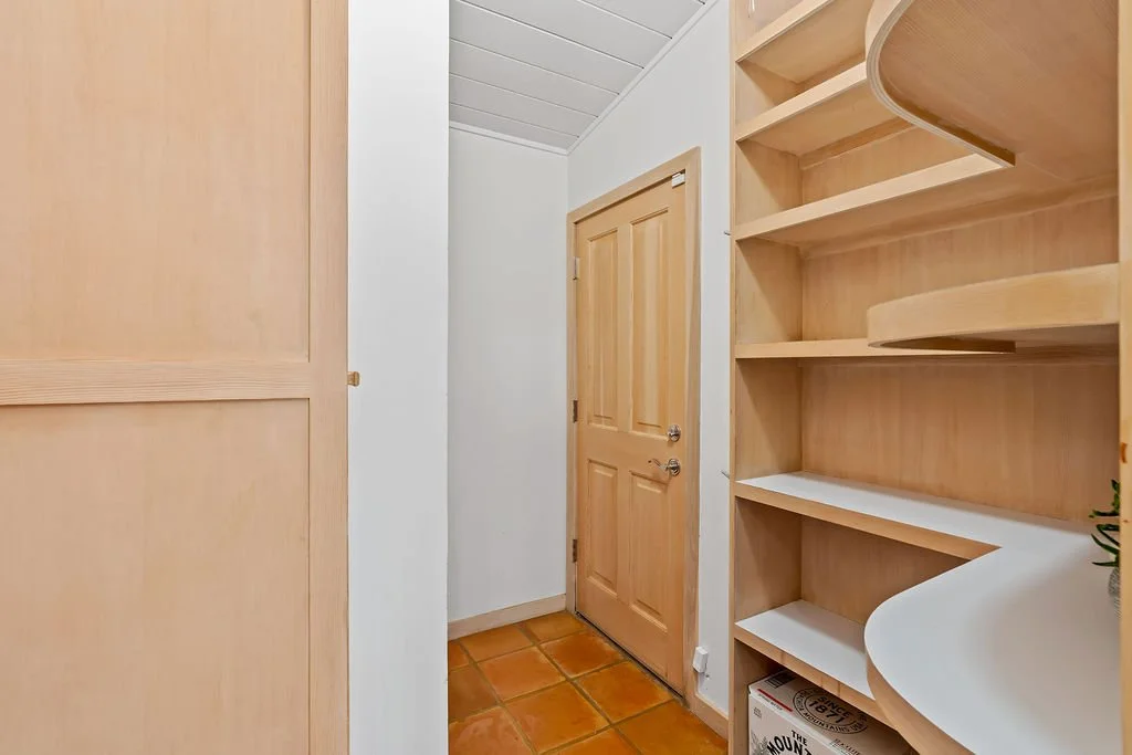 Empty wooden shelves and door in a small room or closet with terracotta tile flooring.