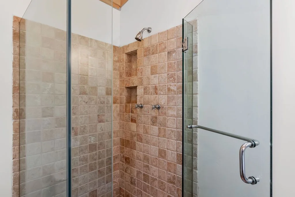 Bathroom shower with glass doors, beige and tan tiles, and a metal grab bar.