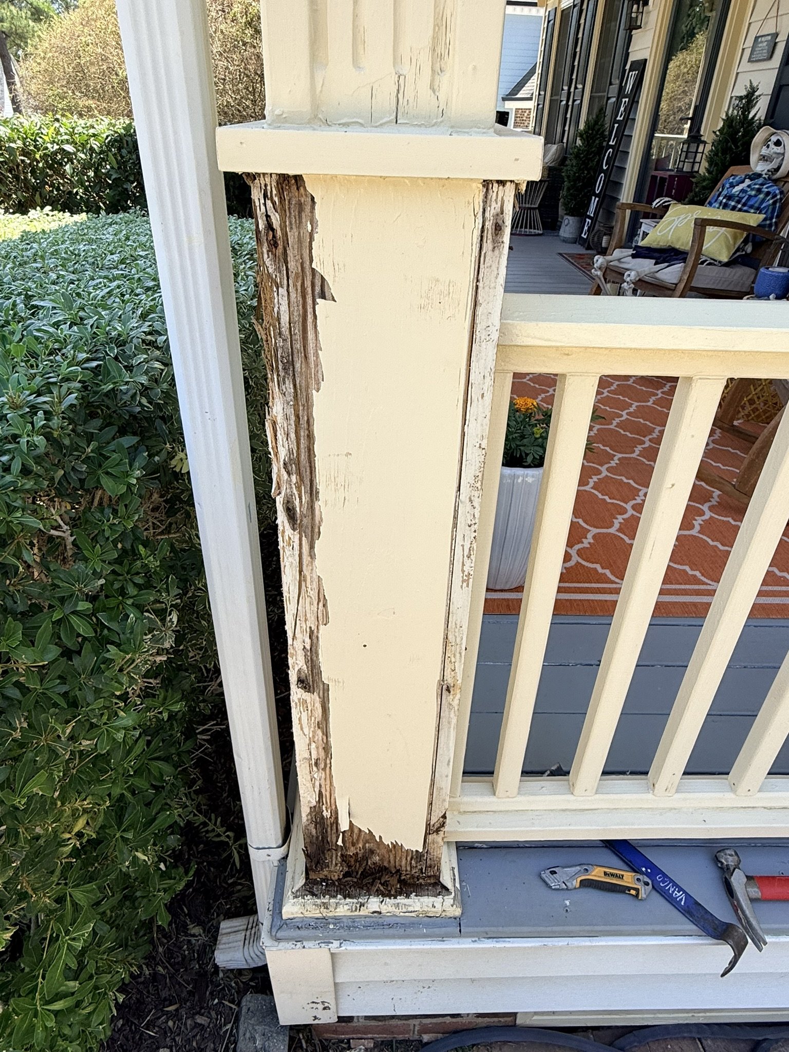 Close-up of a damaged porch post with peeling paint and rot. Tools such as a saw are nearby, suggesting repair or renovation work.