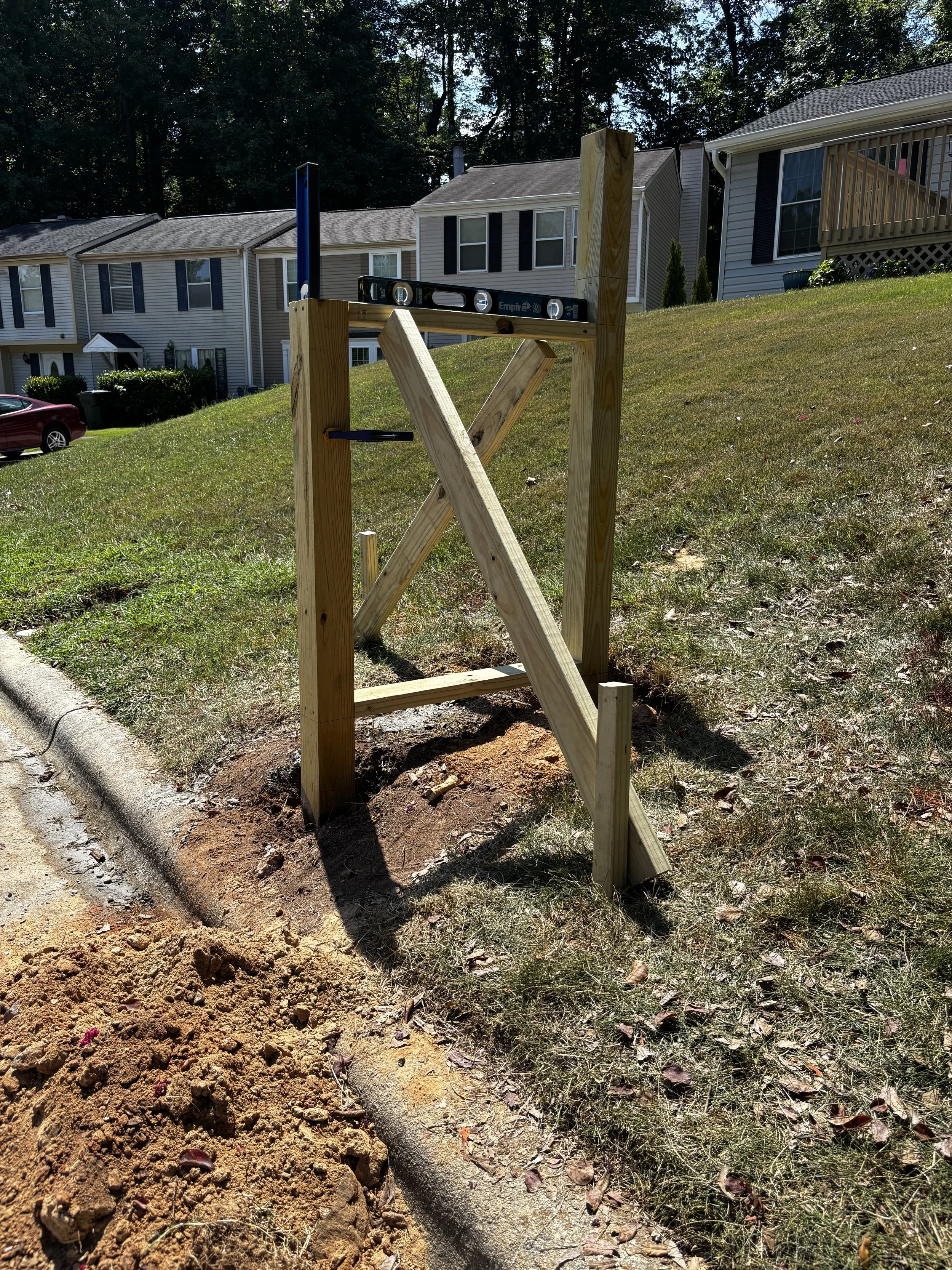 Wooden 4x4 post being installed on a residential lawn, level with a spirit level resting on top, with houses and trees in the background.
