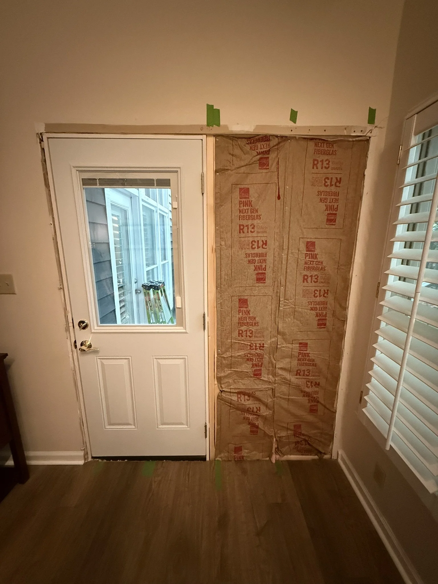Interior view of a door area under renovation, with part of the wall covered in insulation material and a window on the door.