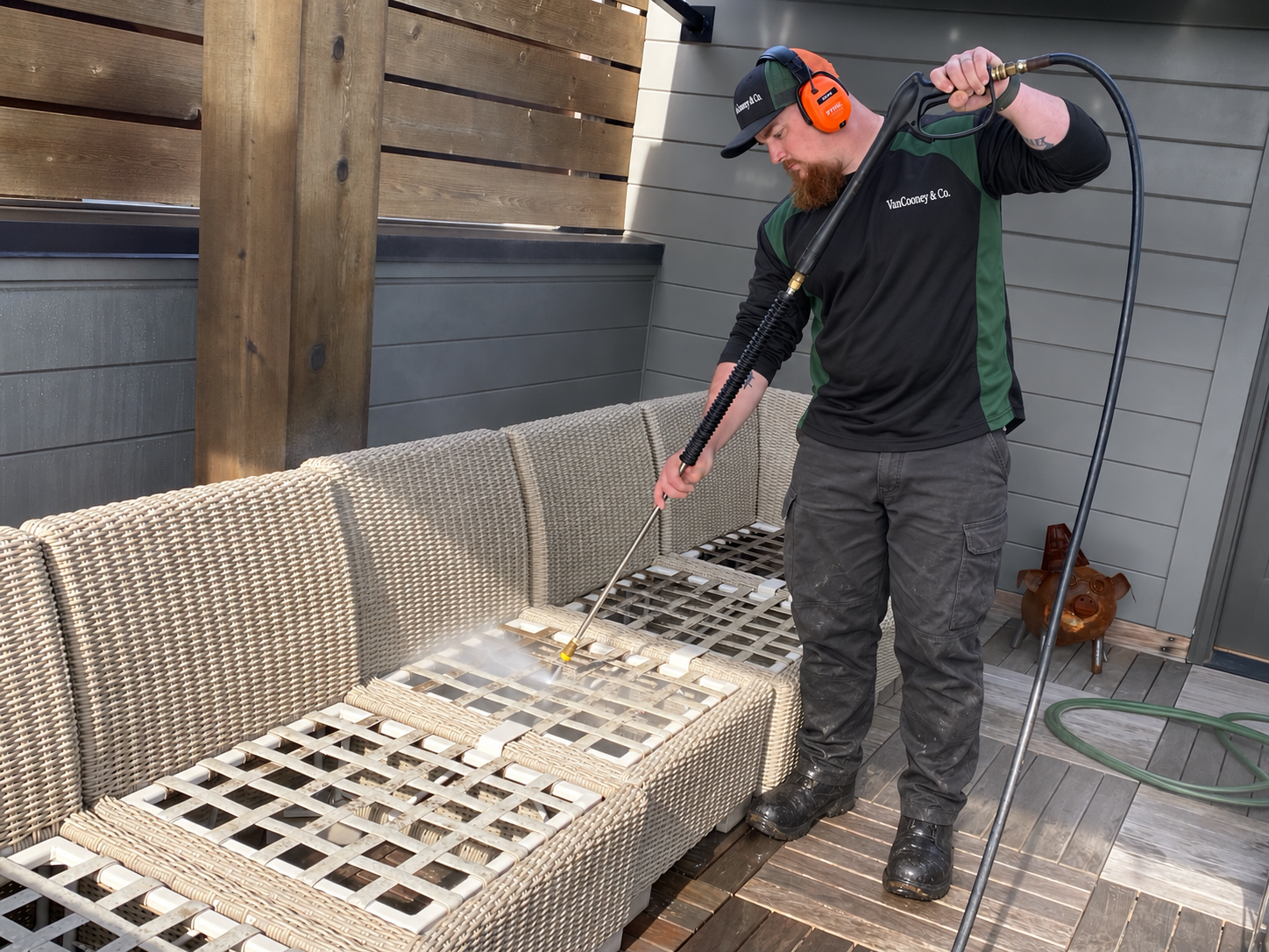 Man using a pressure washer to clean wicker outdoor furniture on a deck.