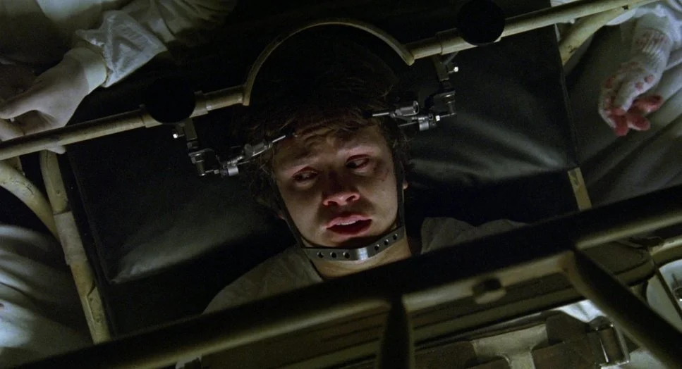 Person strapped to a medical restraint table with a metal neck brace and head immobilizer