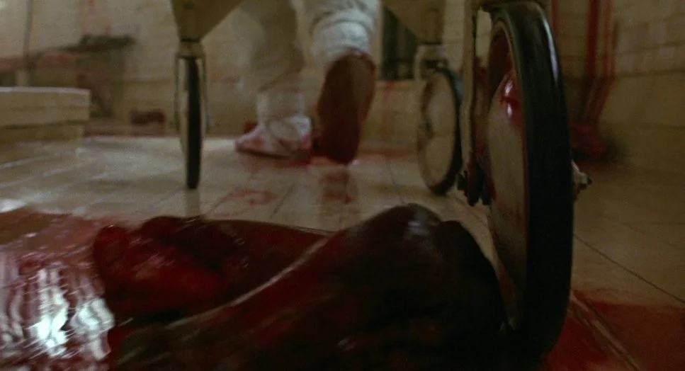 Bloodied body lying on a tiled floor beside a wheelchair
