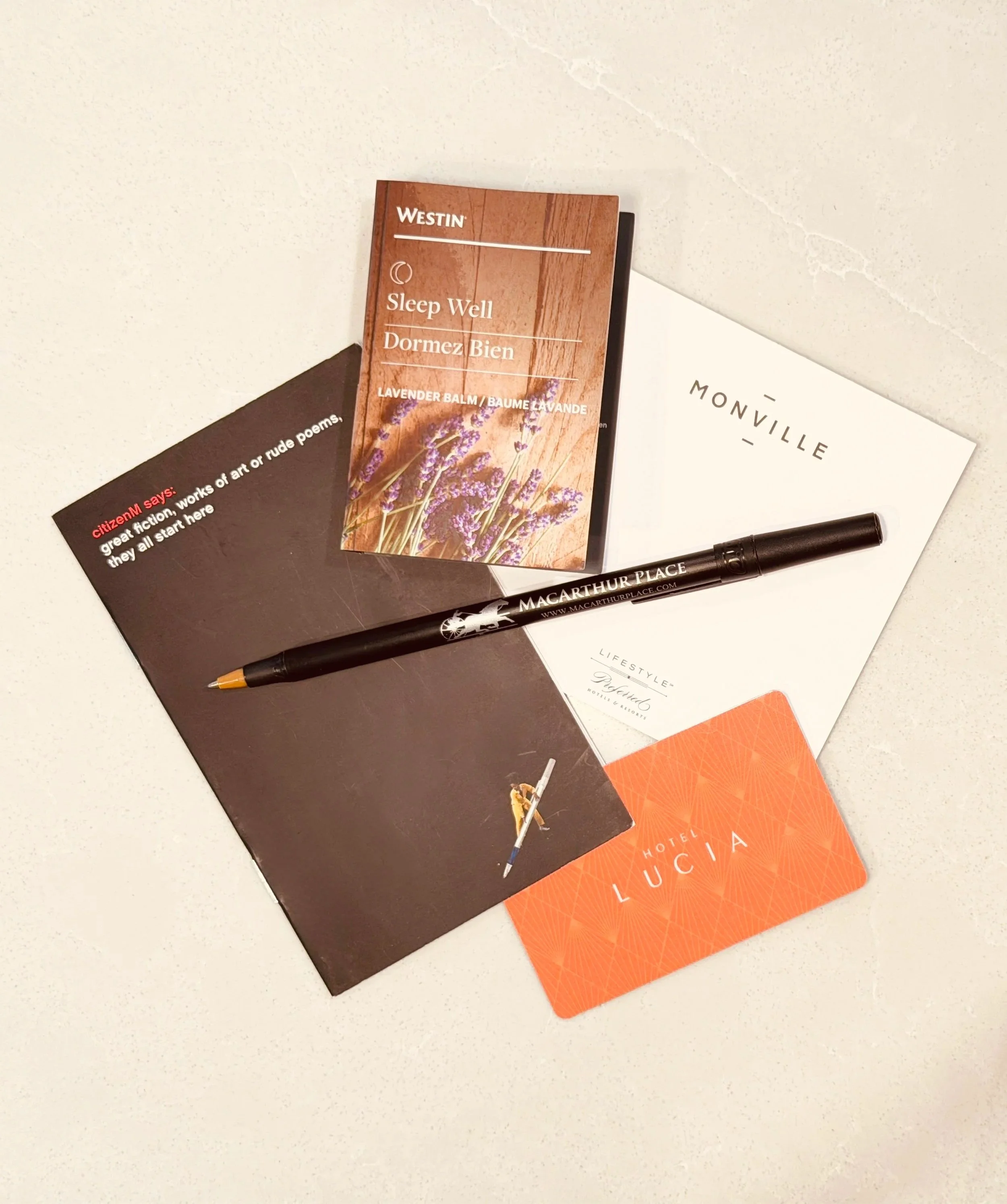 A table with various flyers, a pen, and a card. The flyers include a lavender-themed card reading 'Sleep Well Dormez Bien,' and others with different texts and designs.